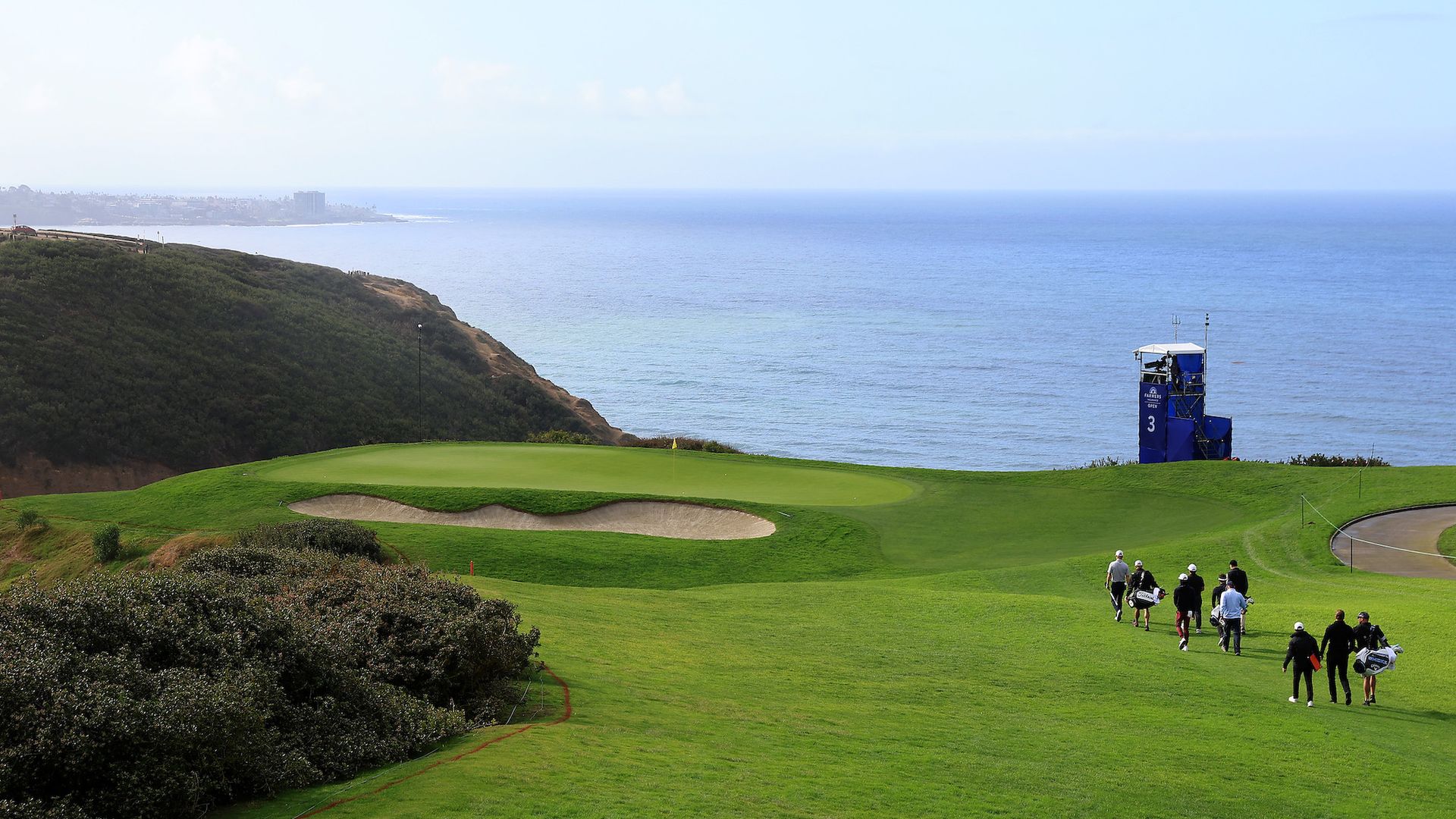 A view of golfers walking towards a hole on the Torrey Pines Golf Course overlooking the ocean. 