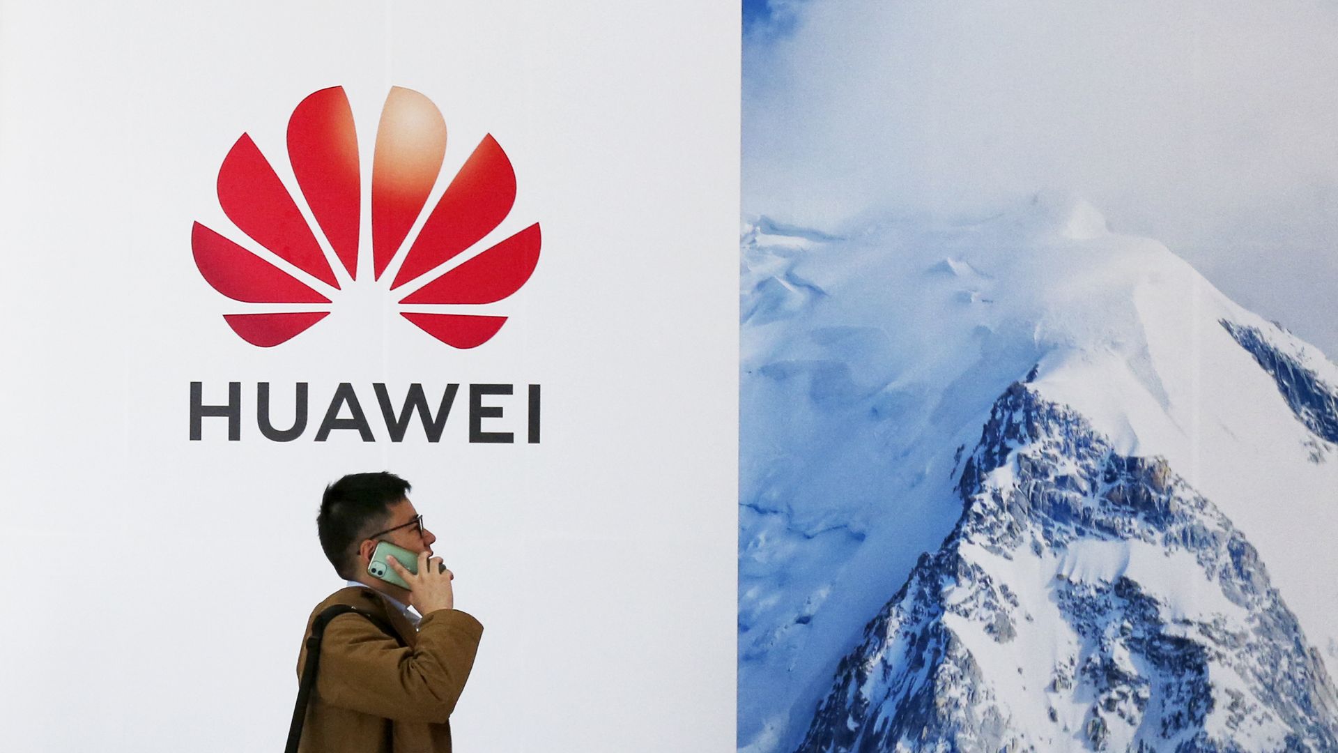 A man walks in front of a wall with the Huawei logo