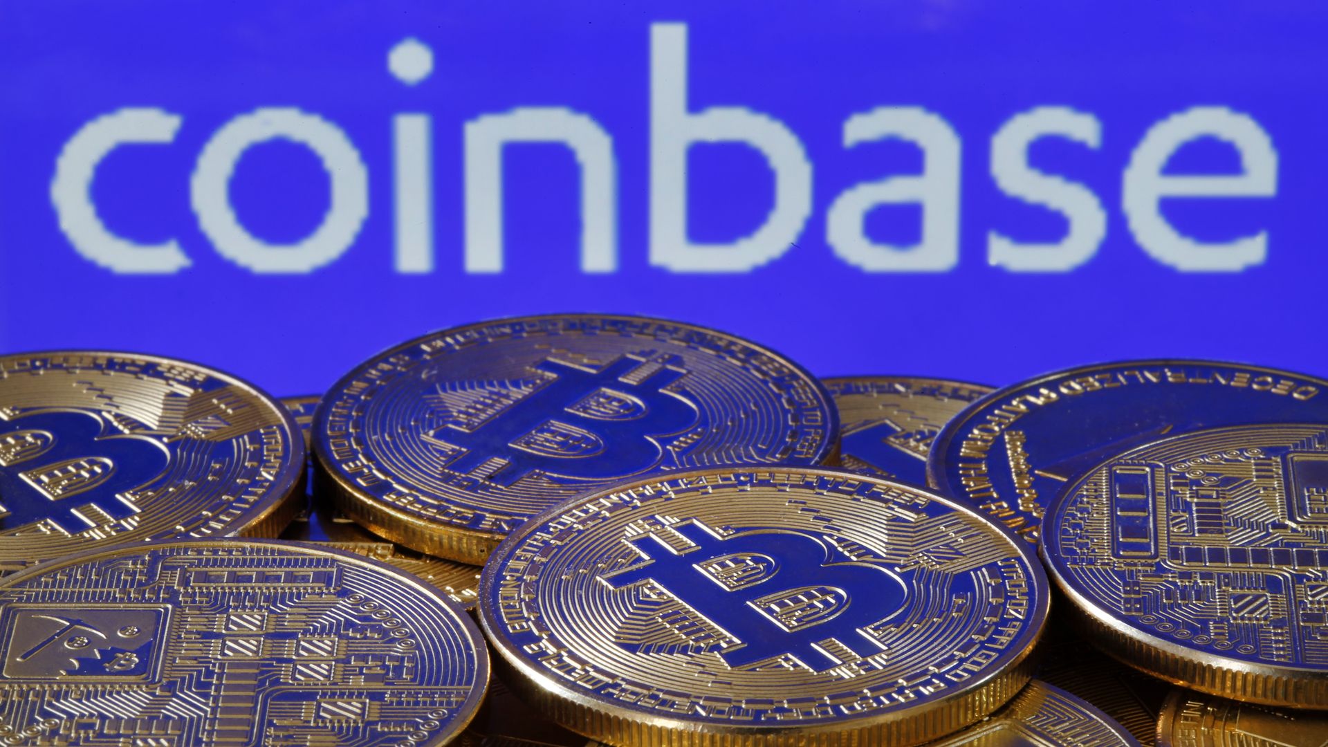 A pile of physical bitcoins in front of a Coinbase sign.