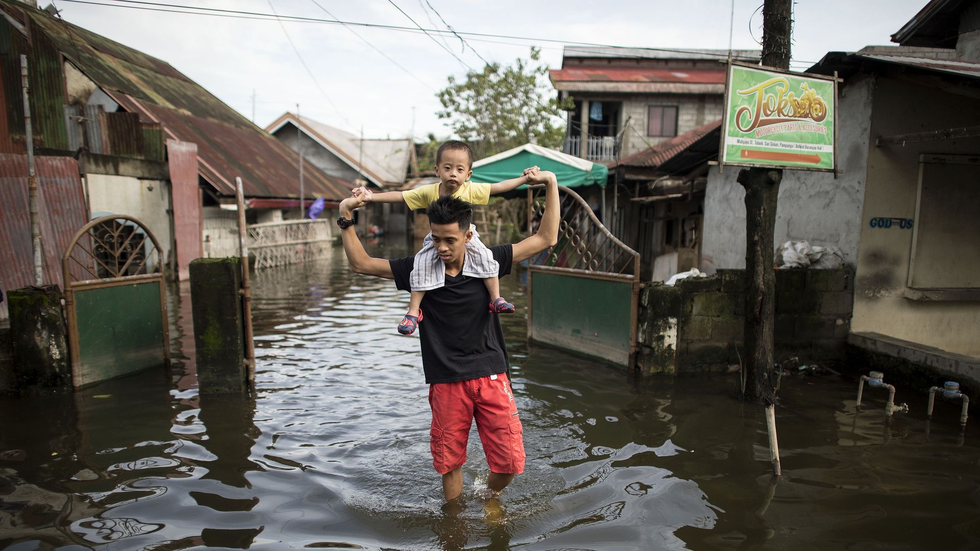 Man carries child on shoulders through flooding