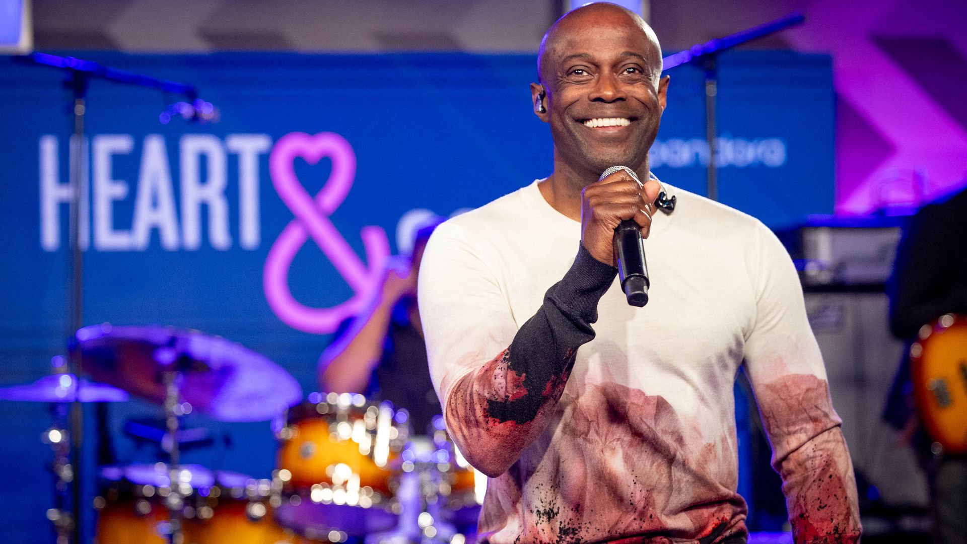 Kem stands with a microphone, smiling