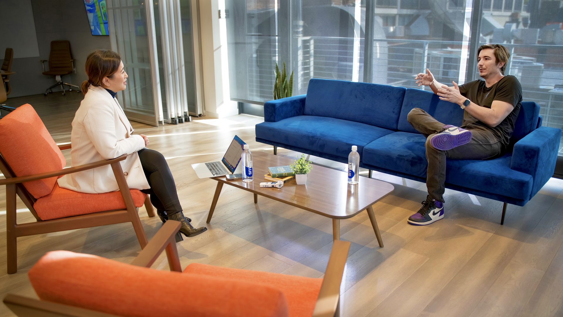 photo of a woman and man talking while sitting on two different couches across from one another, one orange, the other blue