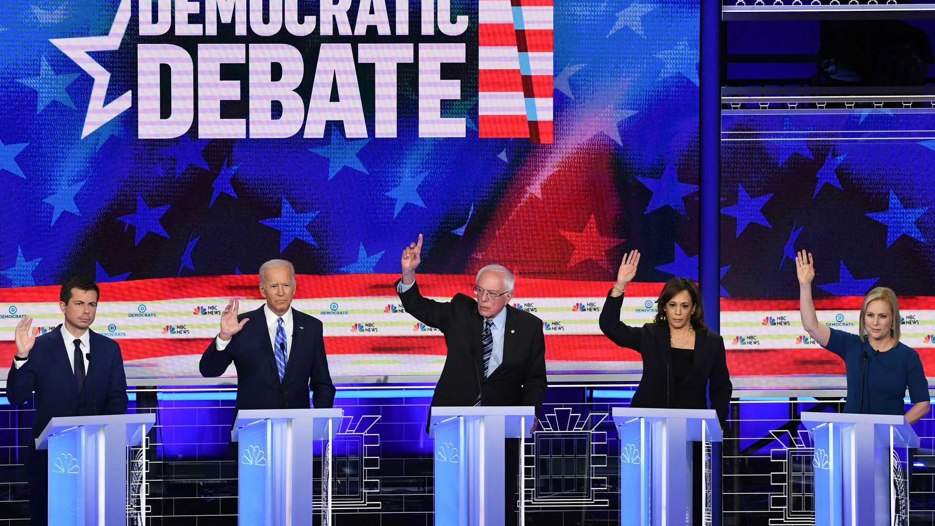 Democratic presidential candidates on the debate stage raise their hands