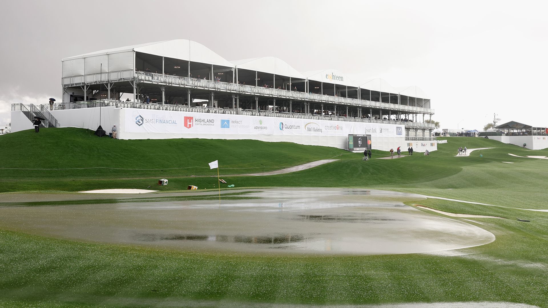 A golf course with pooled water and rain falling.