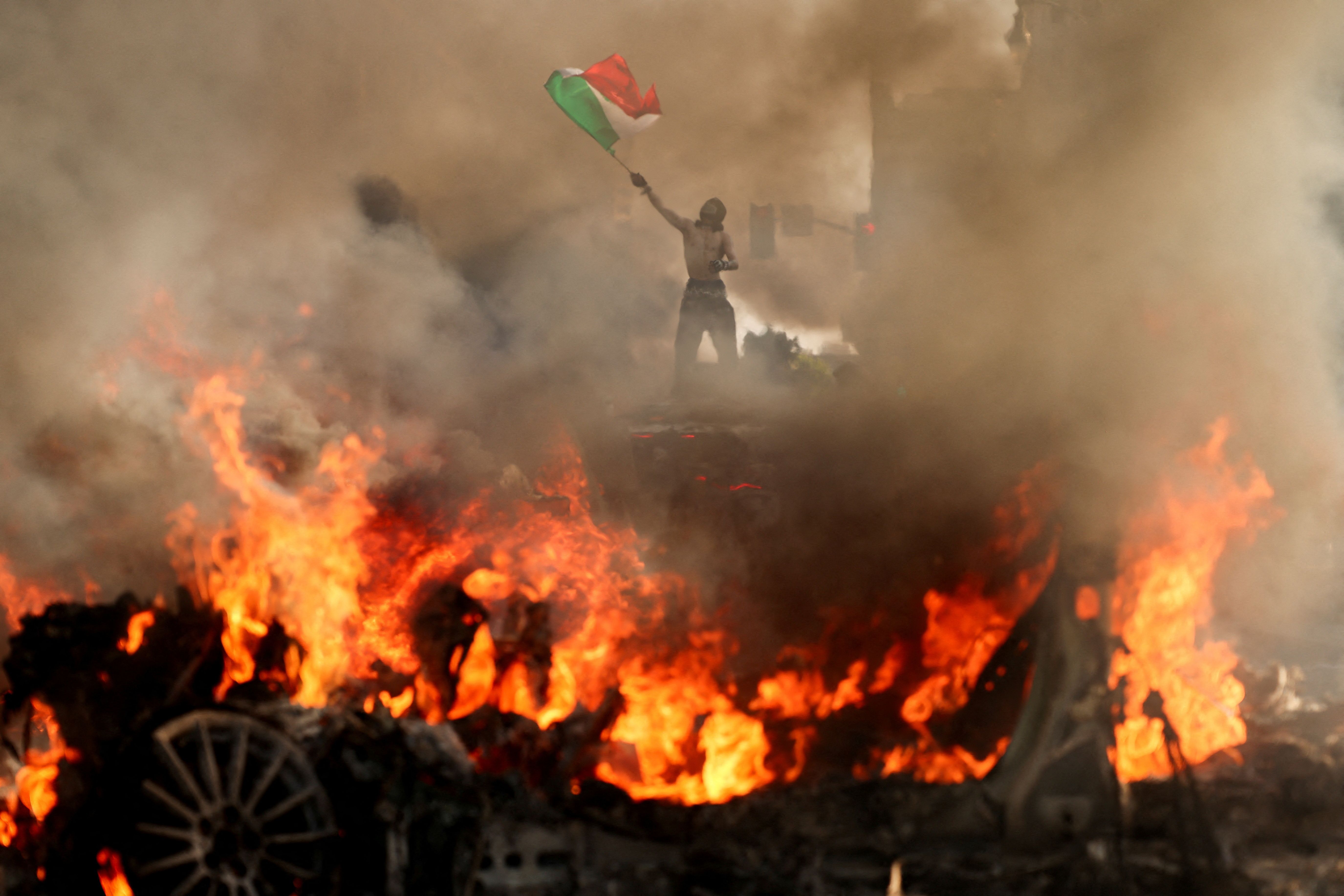 A man waves a Mexican flag in front of burning cars in downtown Los Angeles yesterday.