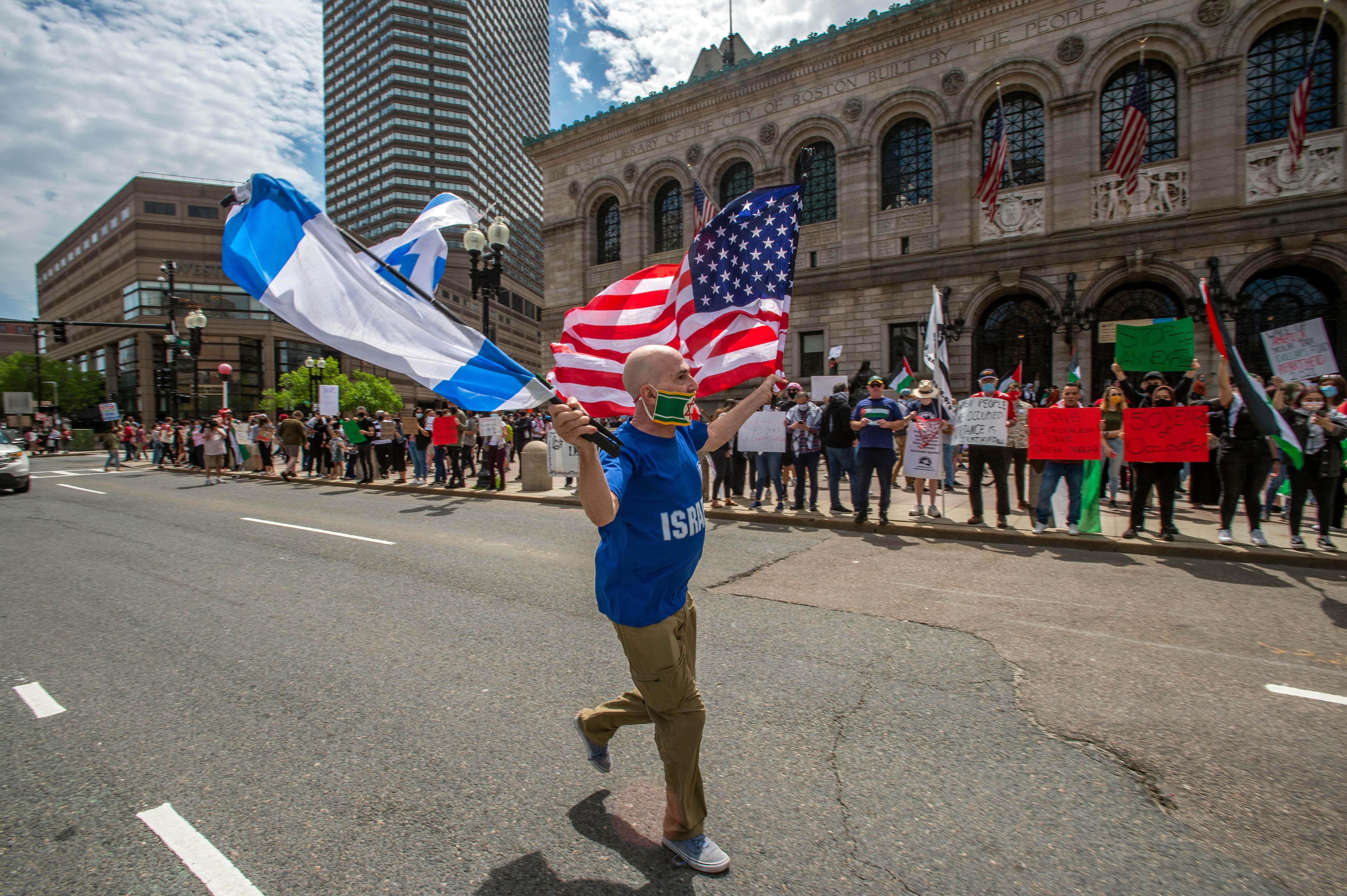 A man, claiming to have been a member of the Israeli army for 32 years, runs waving the flags of Israel and the US at a rally in support of Palestine in Copley Square in Boston, Massachusetts, May 15