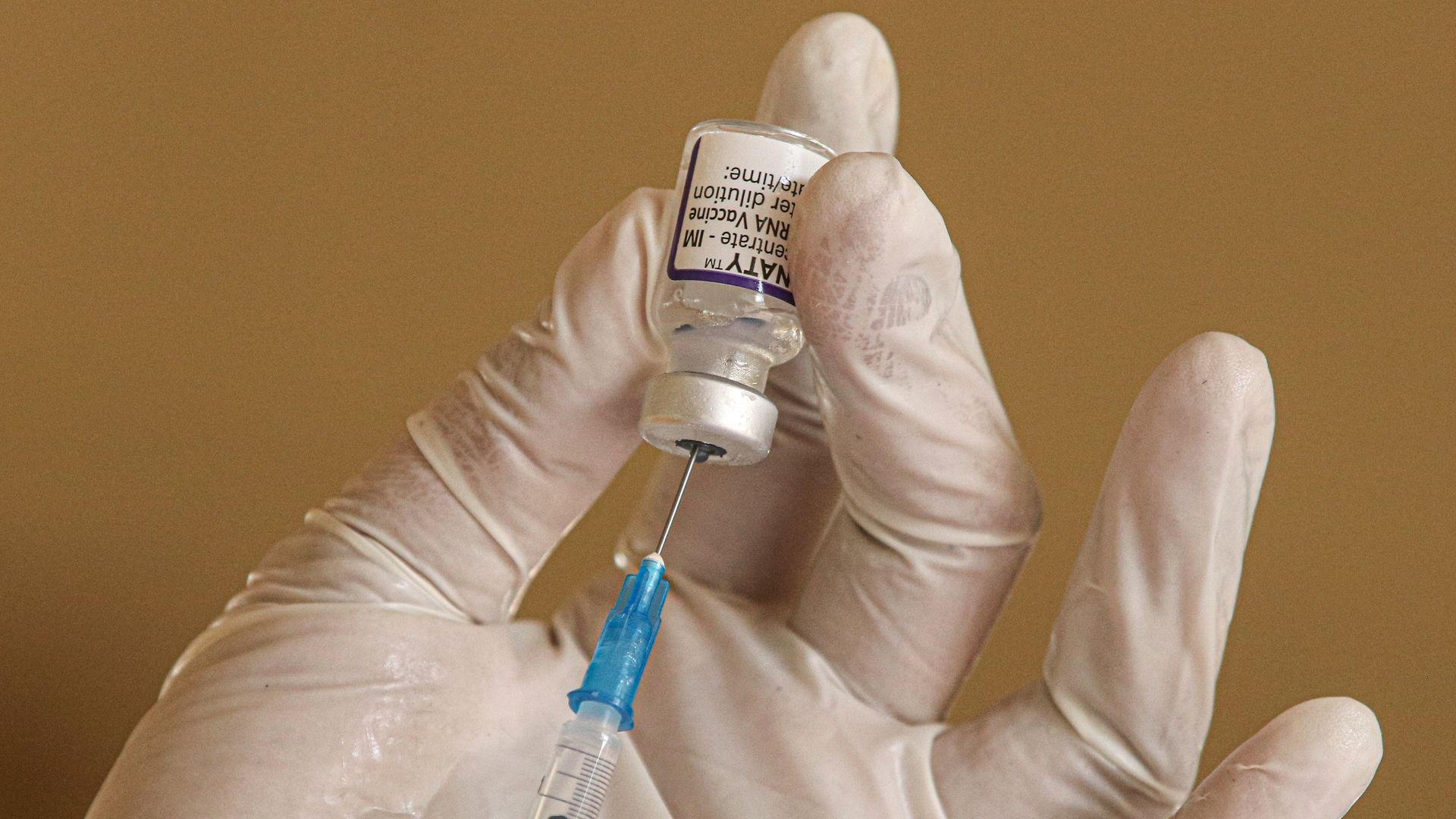 Someone wearing gloves fills up a vaccine syringe