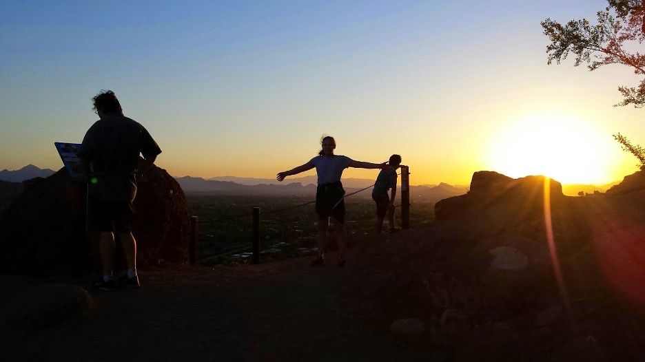 Silhouettes of people climbing a mountain at sunset.