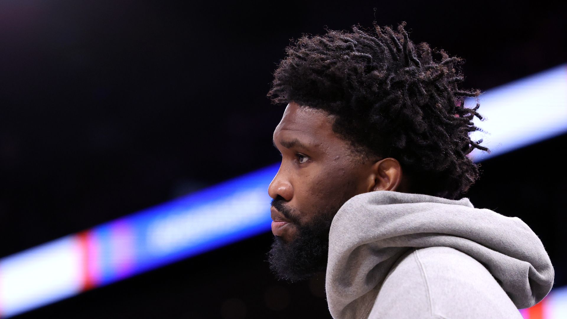 Joel Embiid looks on during a game, wearing a gray sweatshirt.