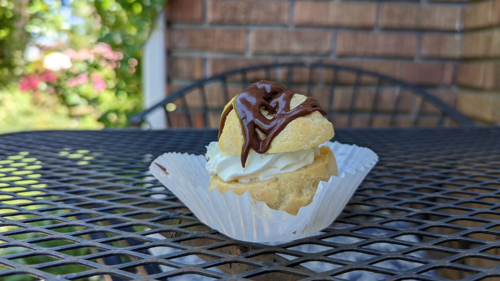 A cream puff is drizzled with chocolate and sitting on a metal table.