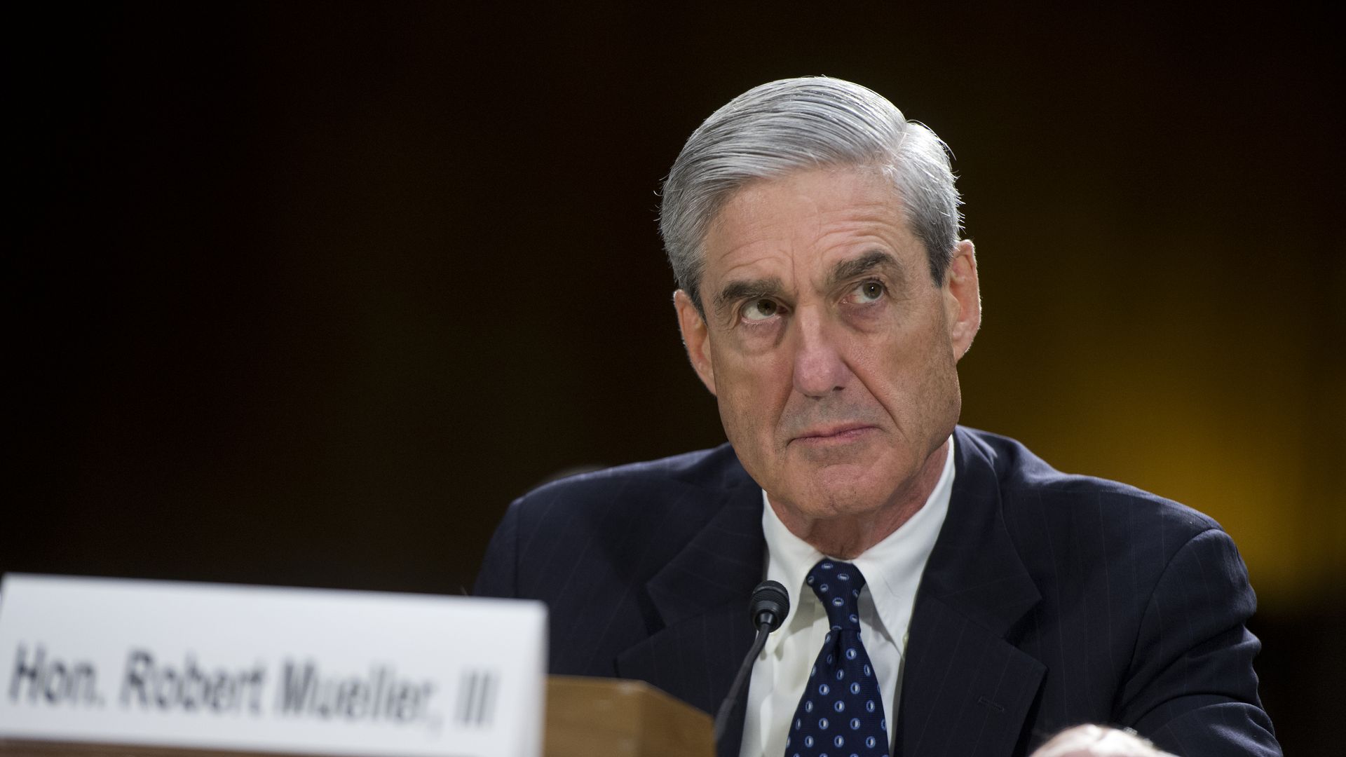 Mueller sits at desk looking stern.