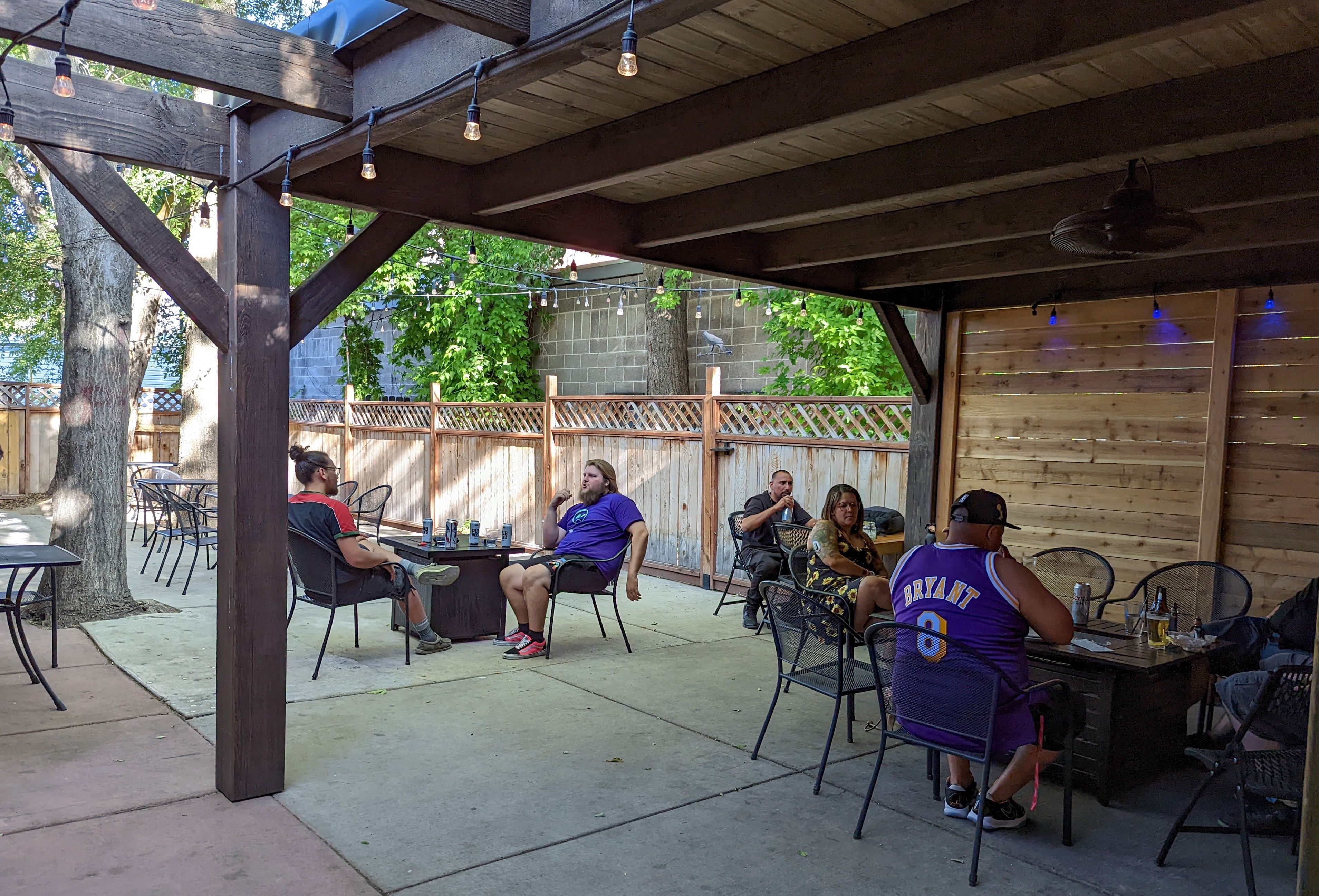 Patrons drink and chat under the porch roof and trees at the Crow and the Pitcher in Murray.
