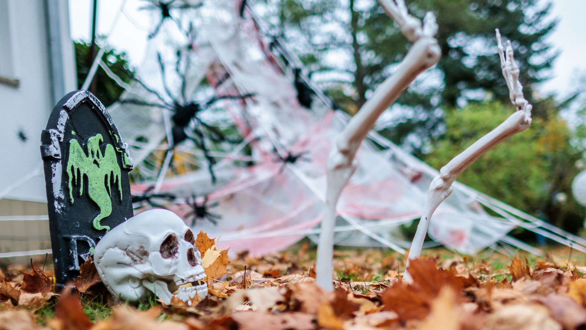 Lawn decorations for halloween. A grave stone with a ghost on it and a skeleton sticking out of some fall leaves.