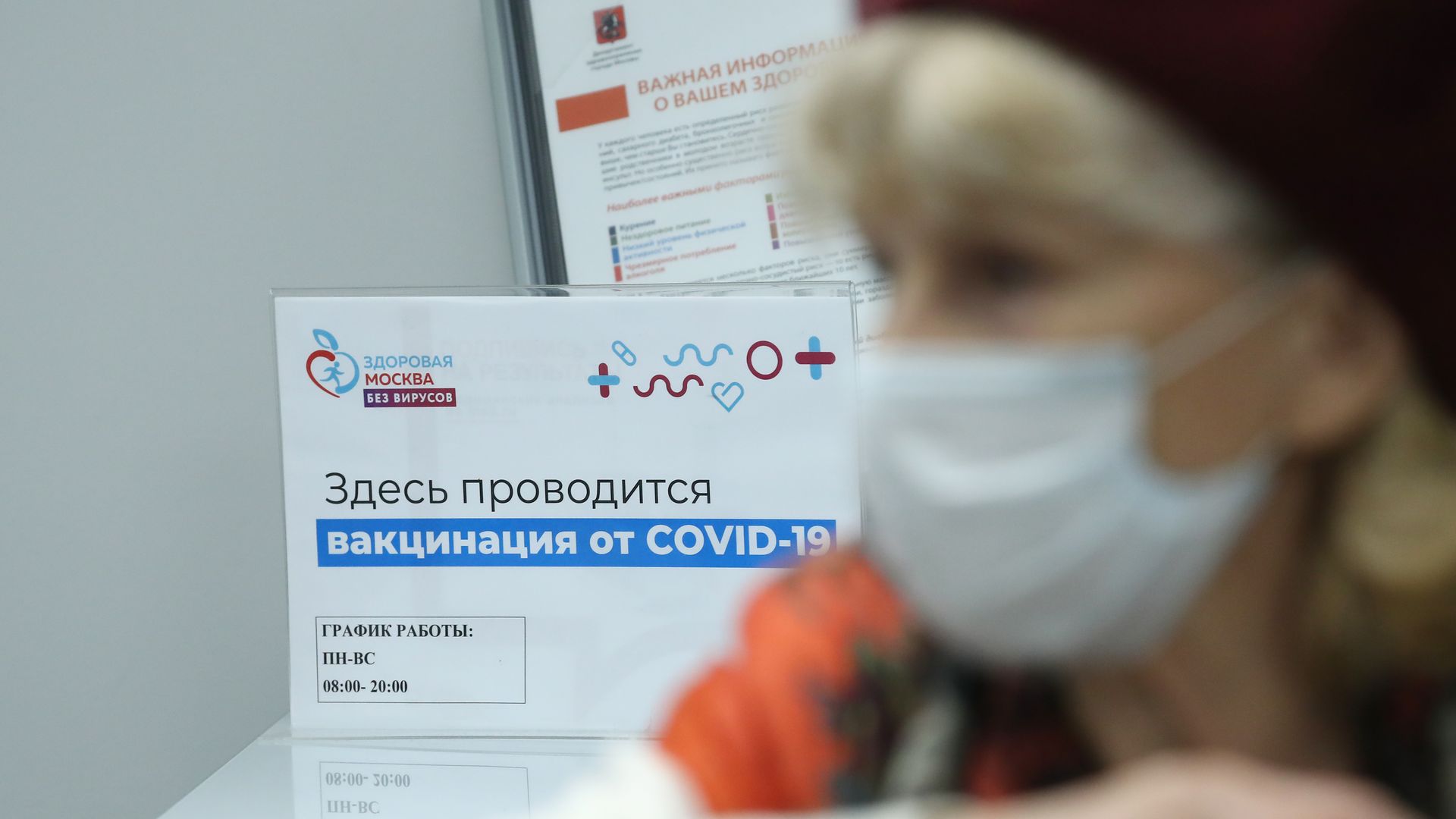 Woman receives a vaccine jab, with a sign behind her in Russian cyrillic 