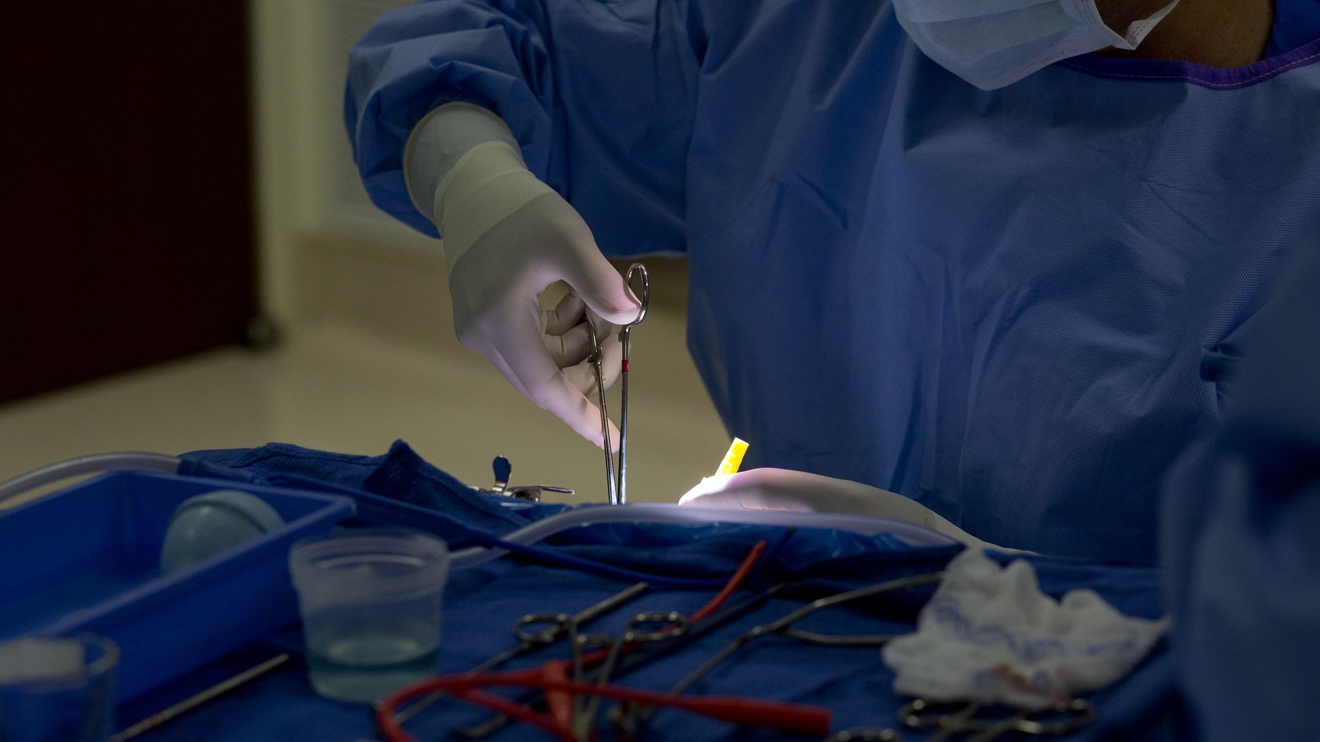 A surgeon uses surgical tools on a patient in a hospital operating room.