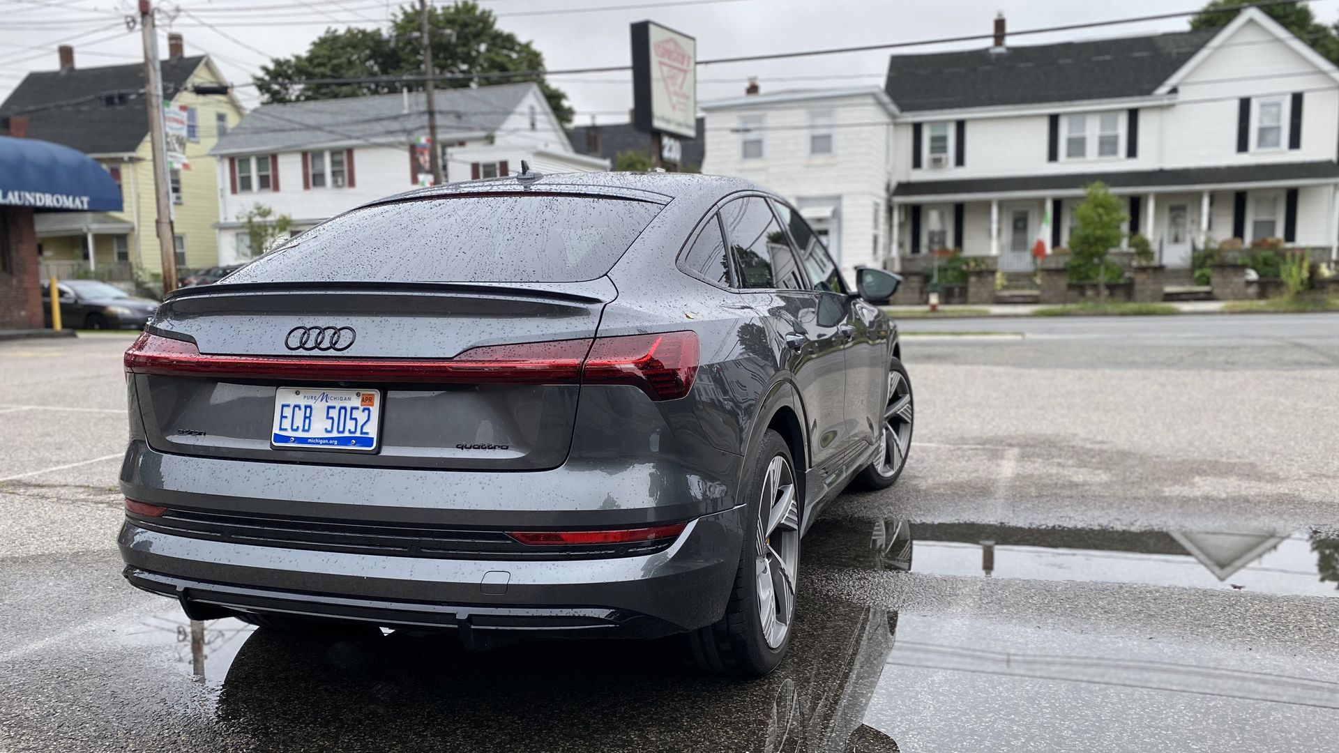 A photo of a gray Audi E-Tron Sportback, taken from the rear of the car, in a parking lot.