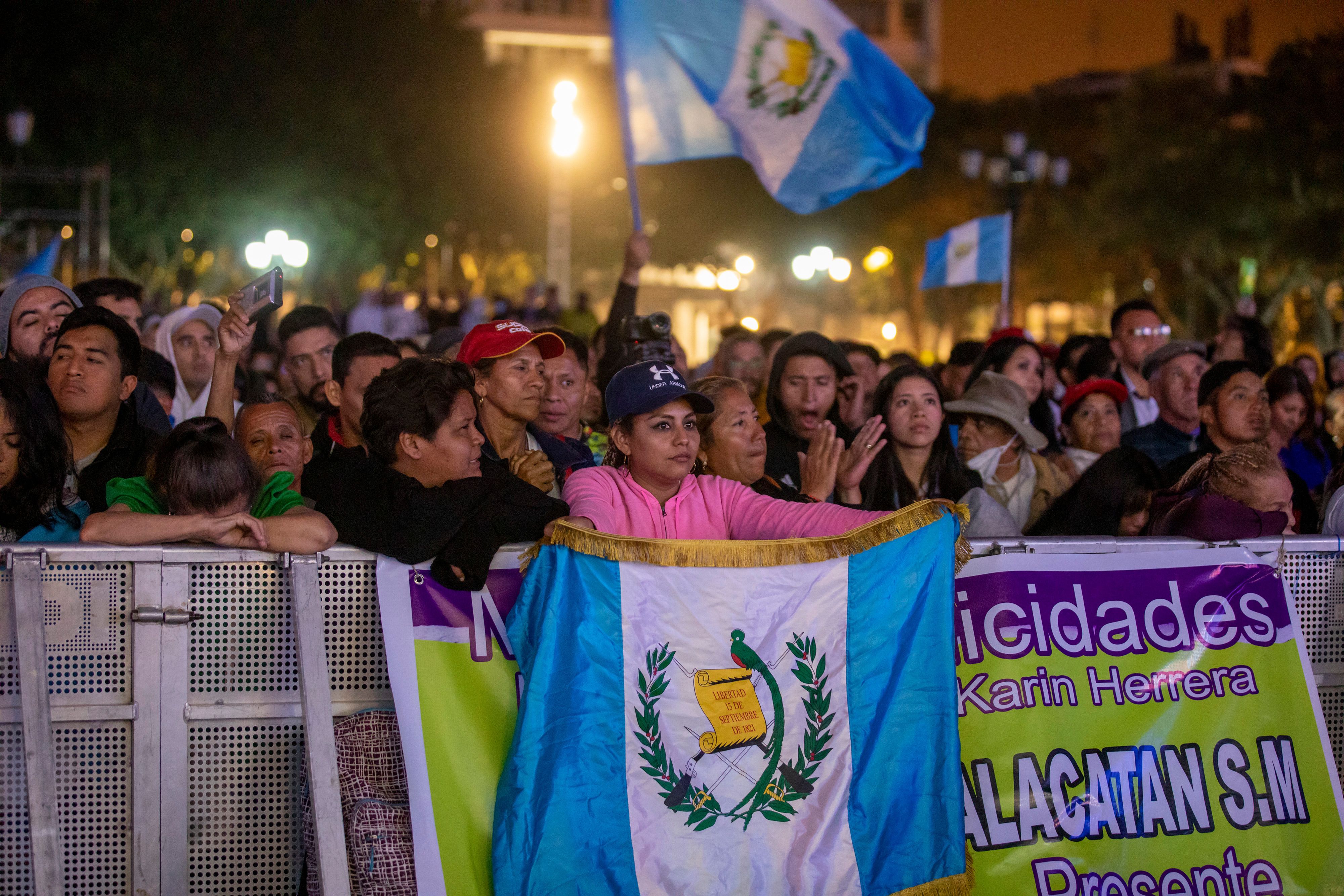 dozens of people are lined up behind barricades. they are waving guatemala flags. 