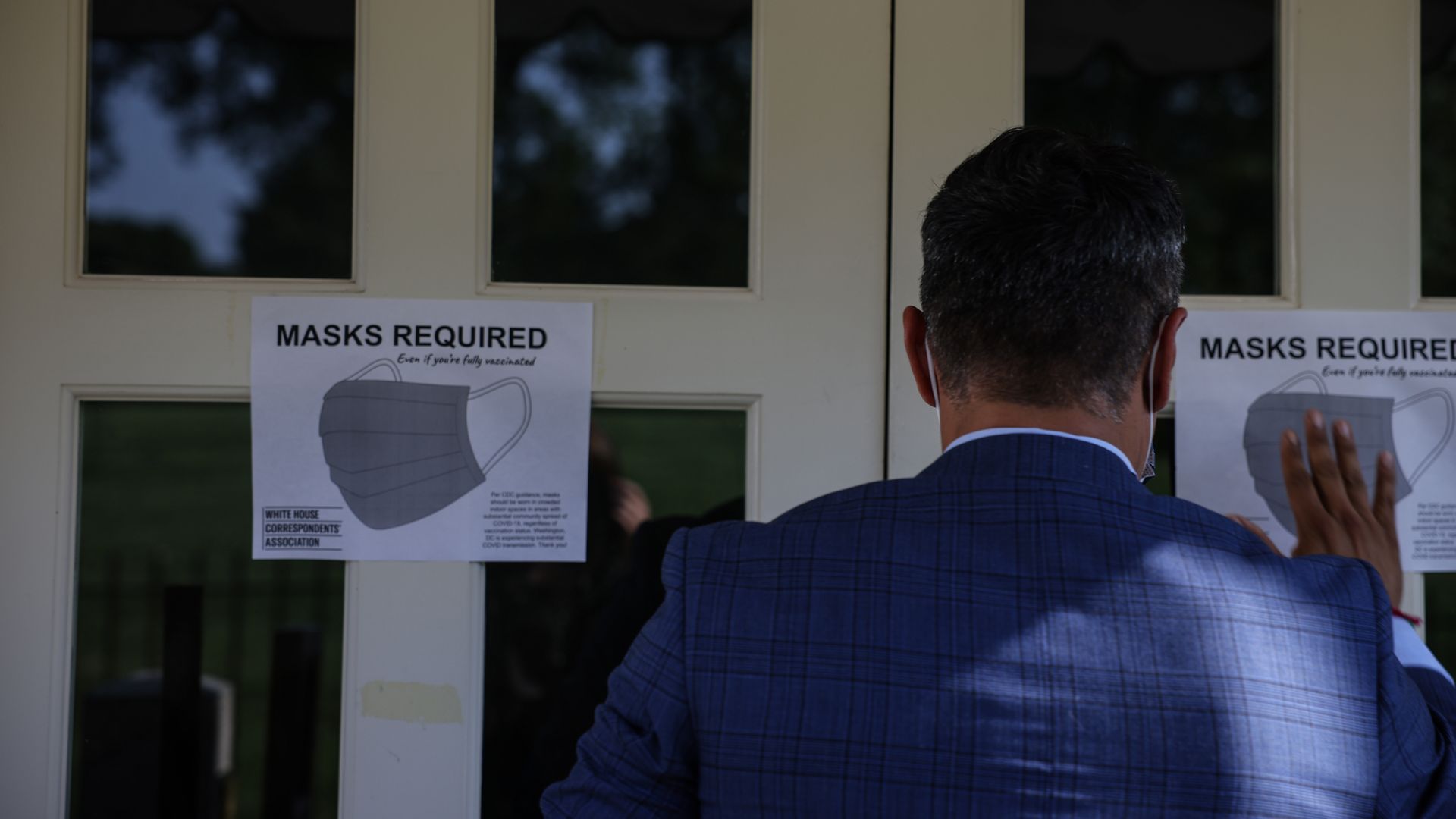 Picture of a man putting up a sign that says "masks required"