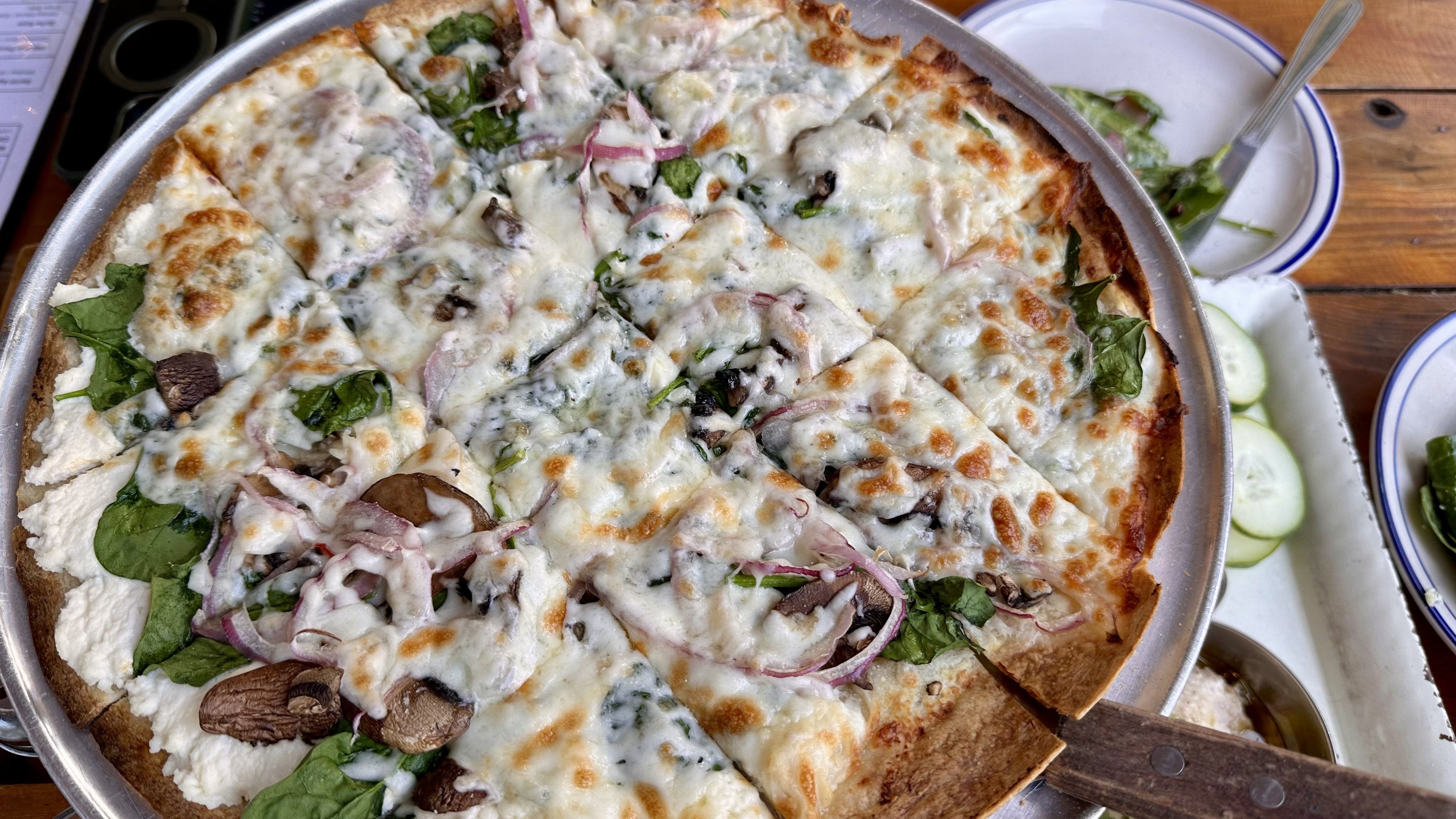 A photo of a large white pizza with mushrooms, spinach and onions on top