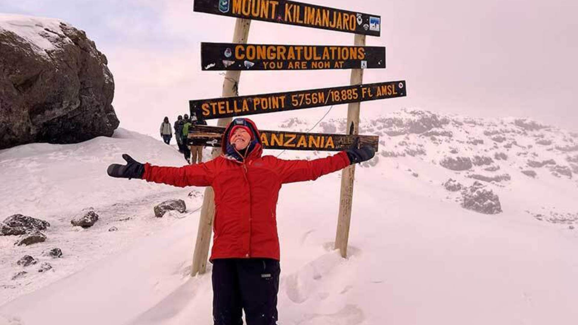  joyful hiker with arms outstretched at Stella Point on Mount Kilimanjaro, celebrating amidst snowy terrain.