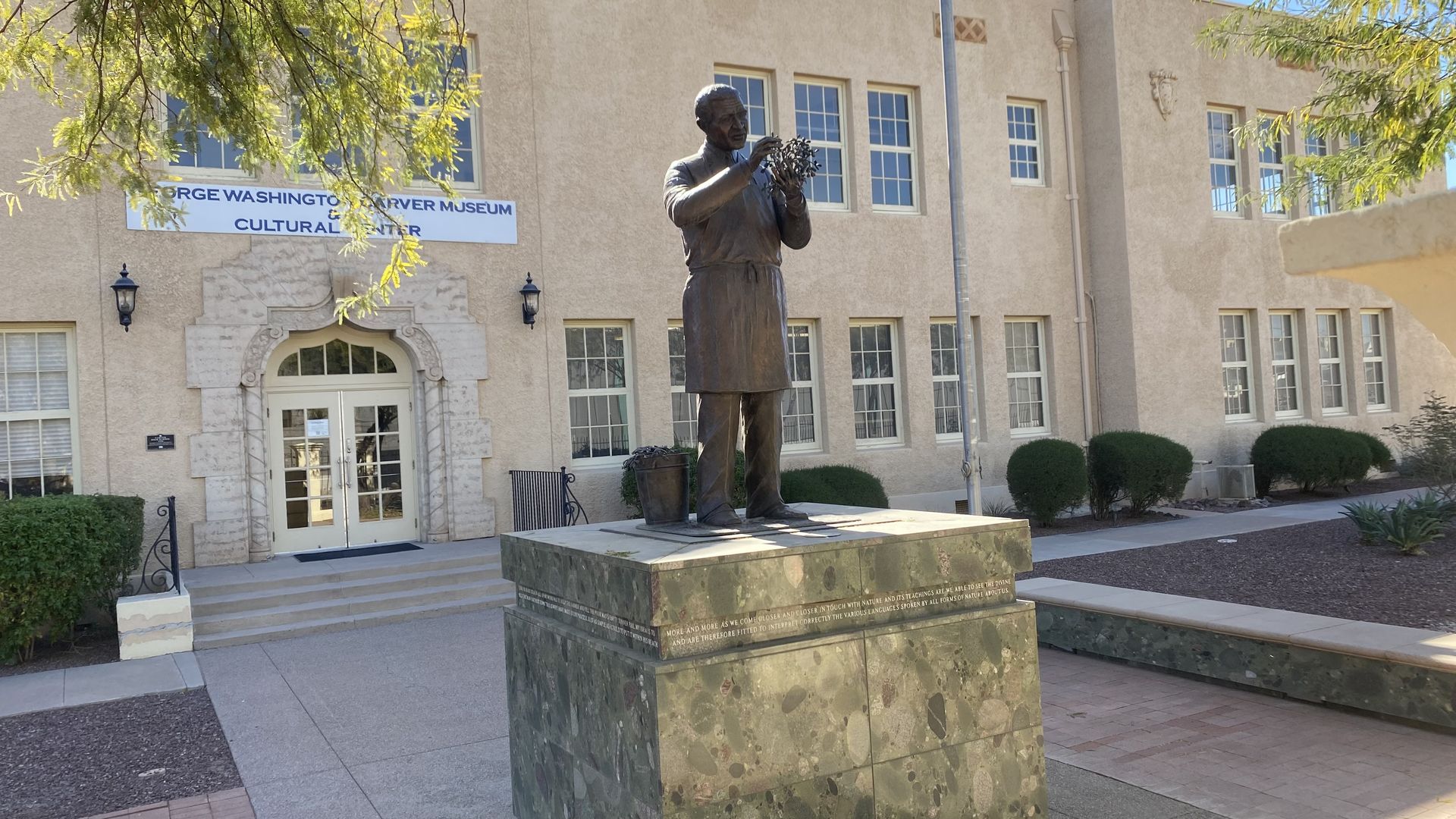 A statute of George Washington Carver on a stone pedestal in front a building with a sign identifying it as the George Washington Carver Museum and Cultural Center.