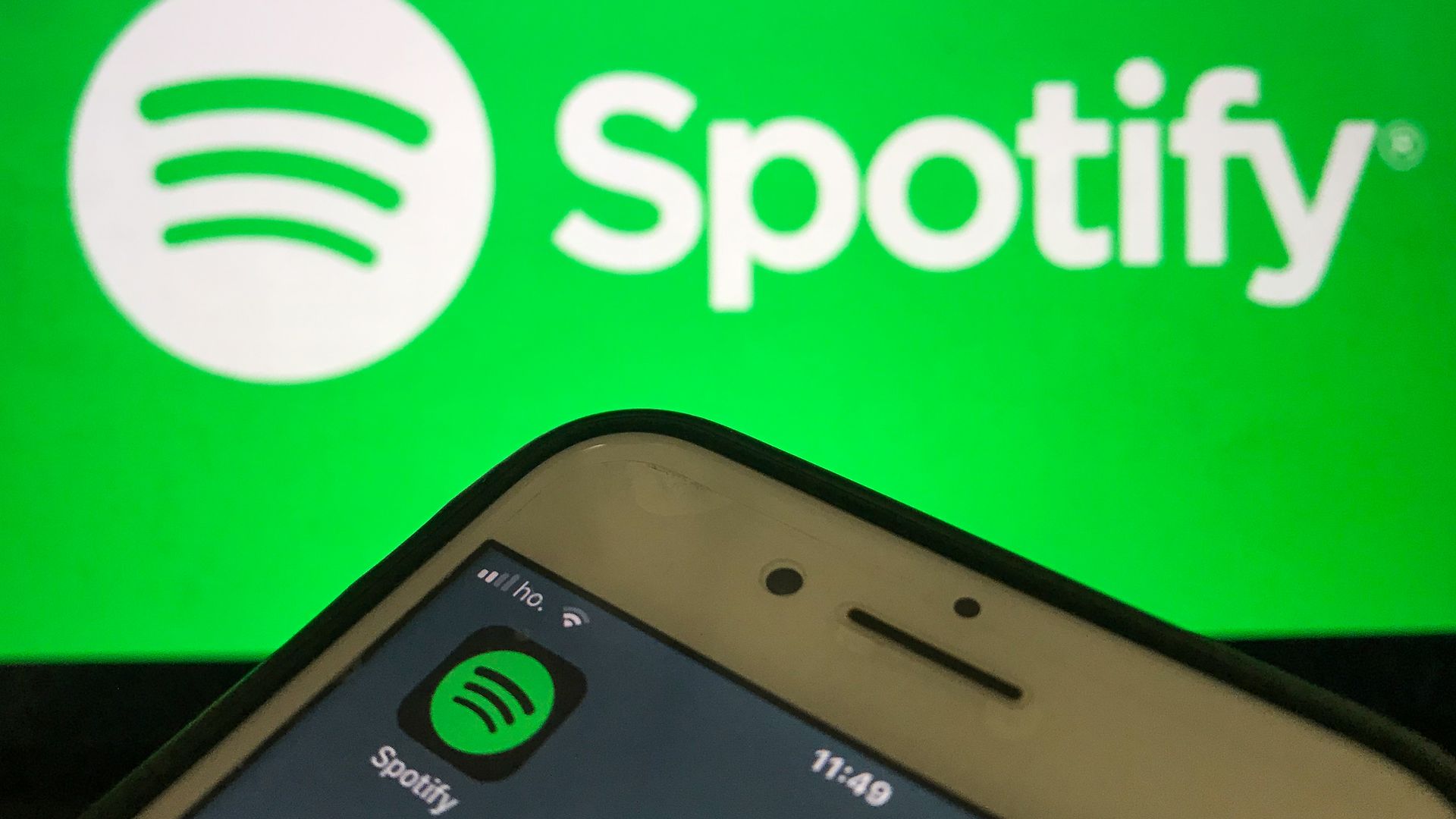 A photo illustration of an iPhone with the Spotify app set against a backdrop of the Spotify logo.