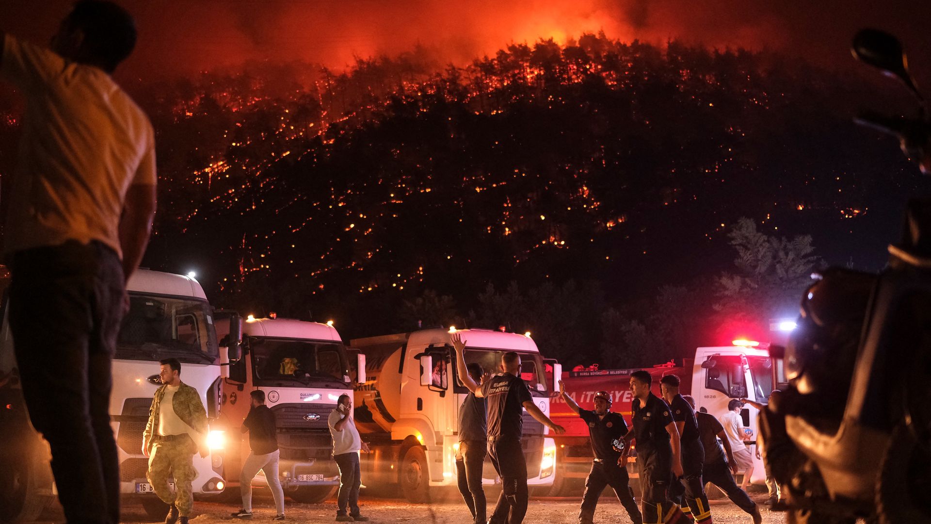 Residents and firefighters attempt to extinguish a wildfire as smoke and flames rise from a forested area in the Gursu district of Bursa early on July 27, 2025.