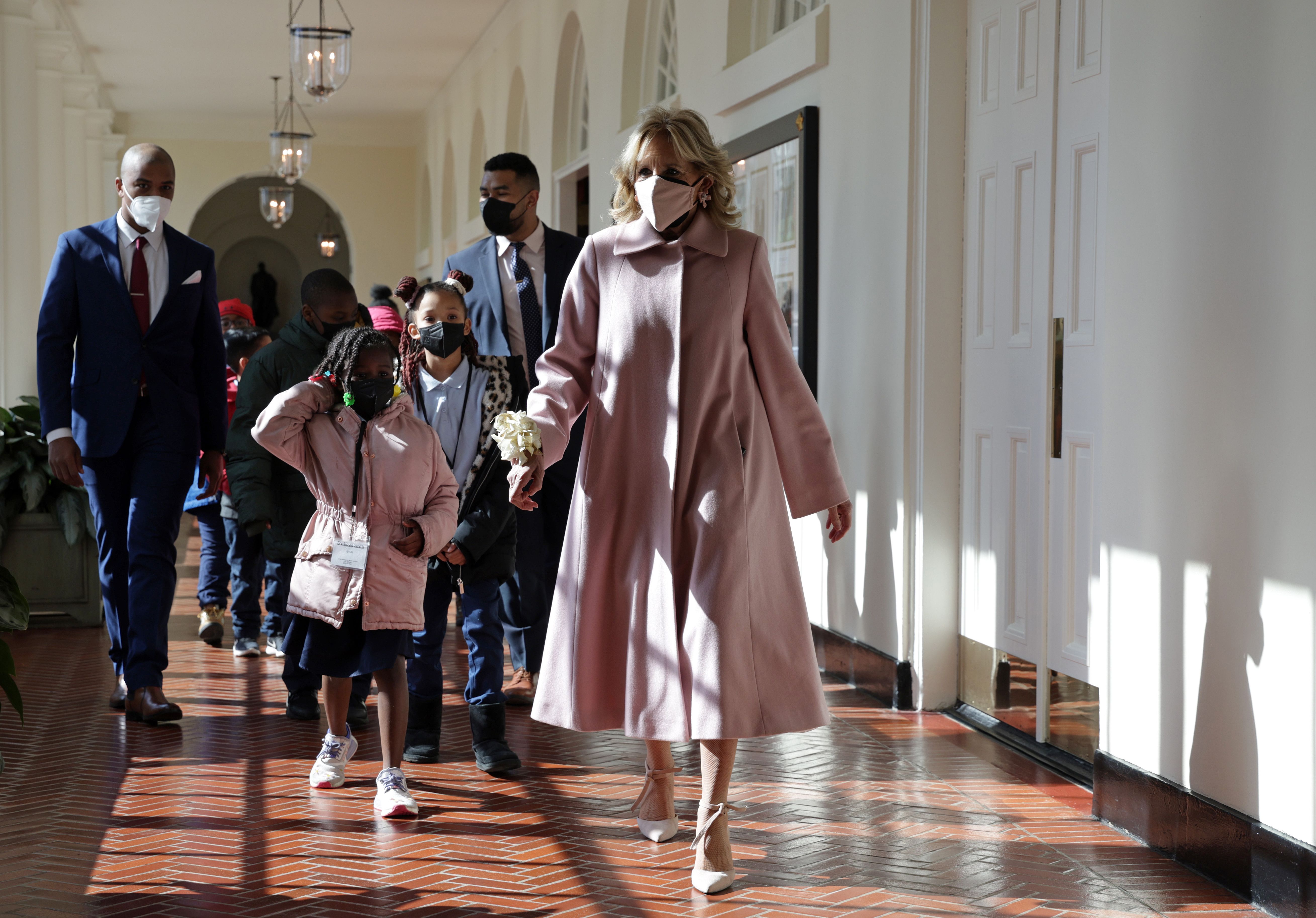 First lady Jill Biden, wearing a long, pink coat and matching face mask leads a tour of similarly masked with second graders in 2022.