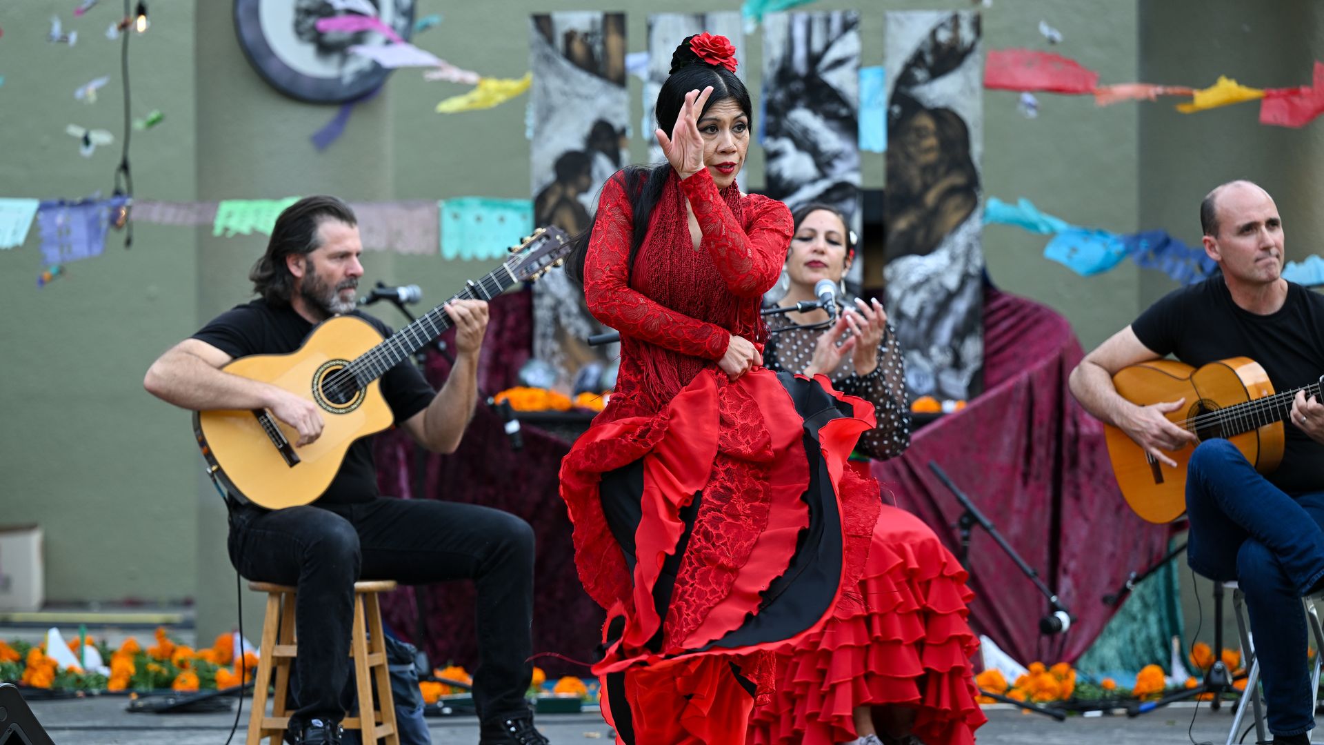 Photo of a Latina woman dancing in a red dress as people strum guitars behind her