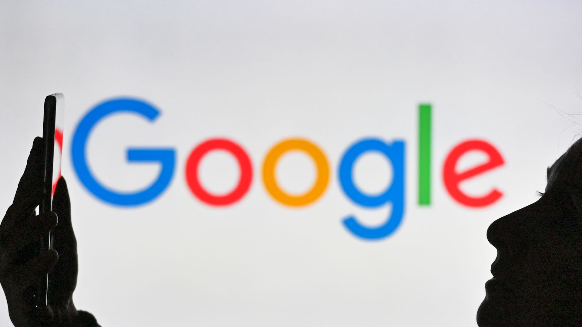Picture of Google logo with a person standing in front of it holding a phone