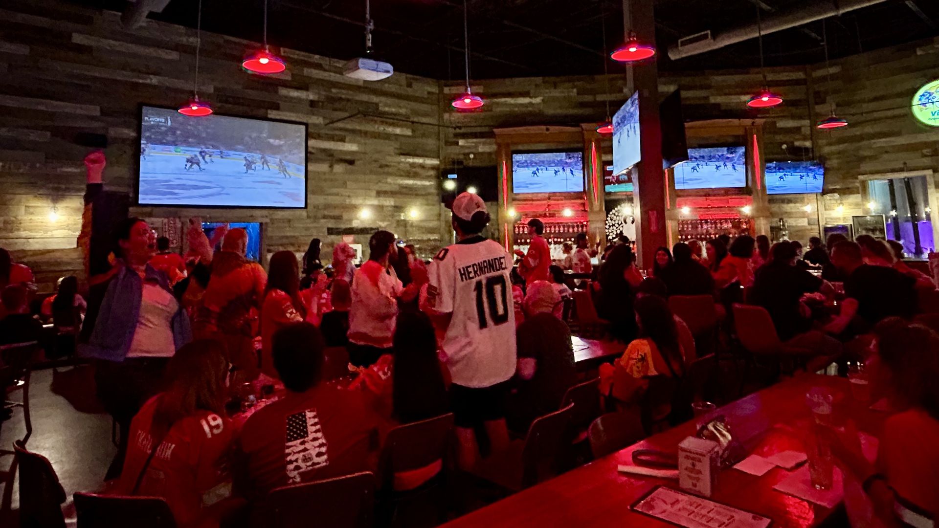 A group of people watching the hockey game on a large TV screens.