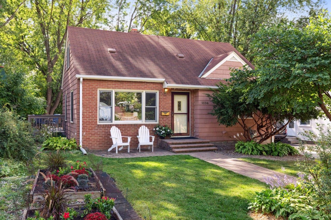 brick red home with white porch chairs and greenery
