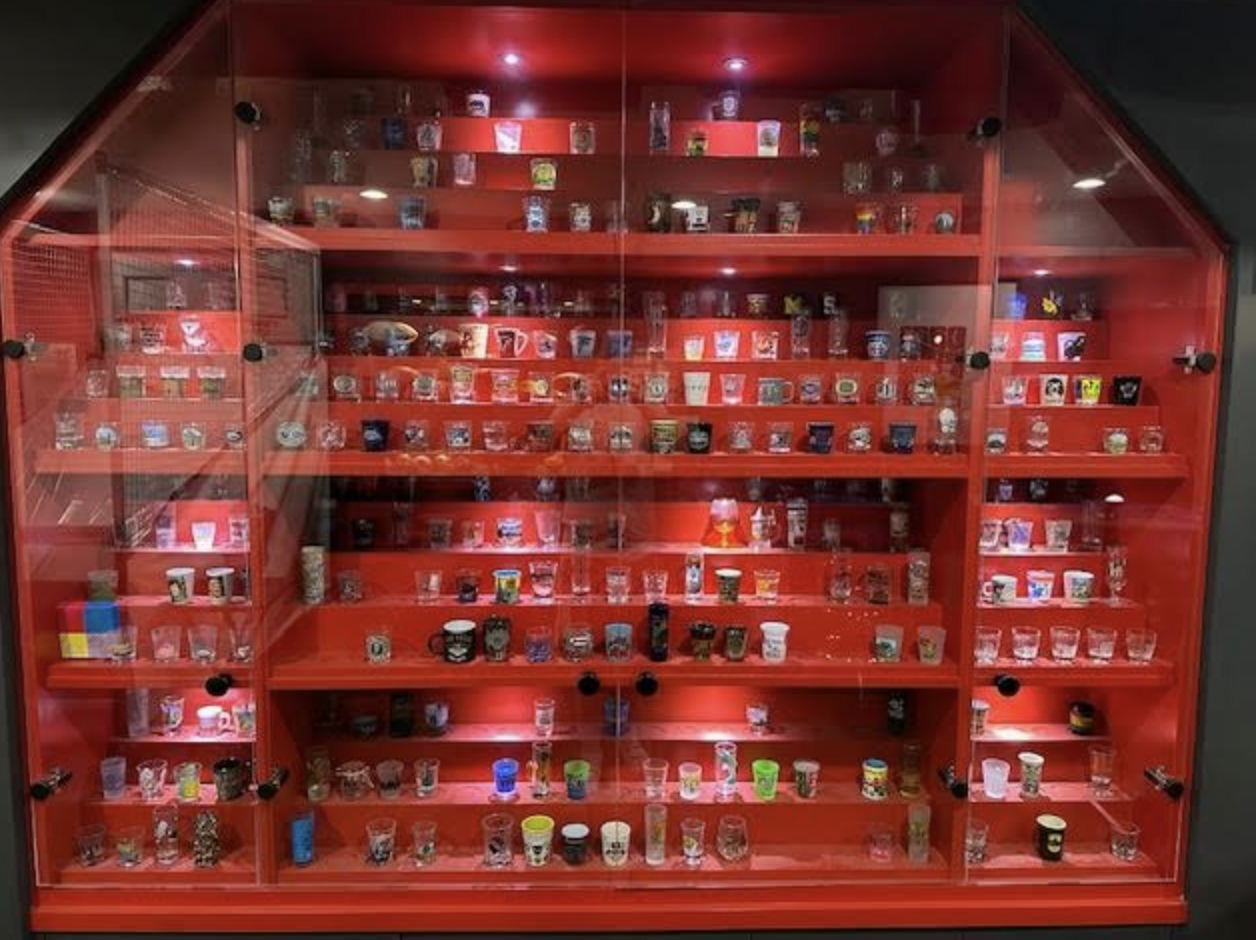 A red display case featuring many shot glasses