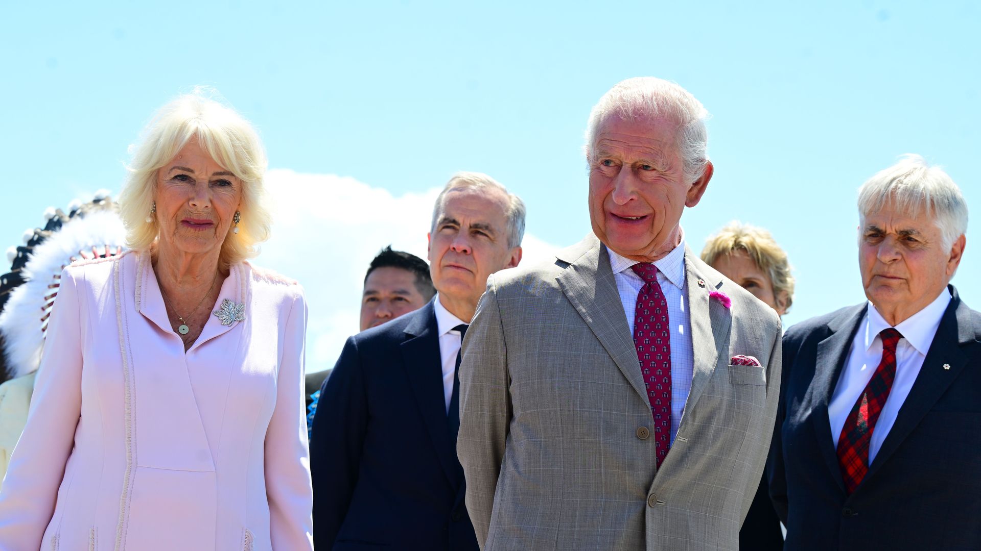 Queen Camilla stands to the left wearing pink, next to Mark Carney wearing a dark suit, next to King Charles wearing a gray suit 