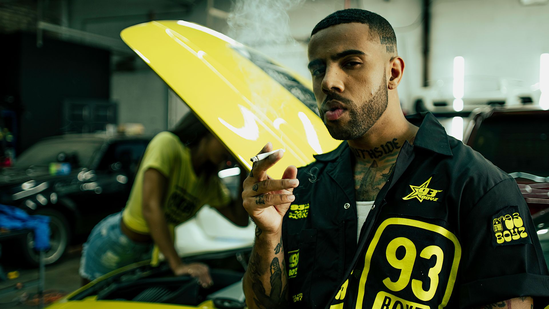 Photo of a man smoking in front of a car. 