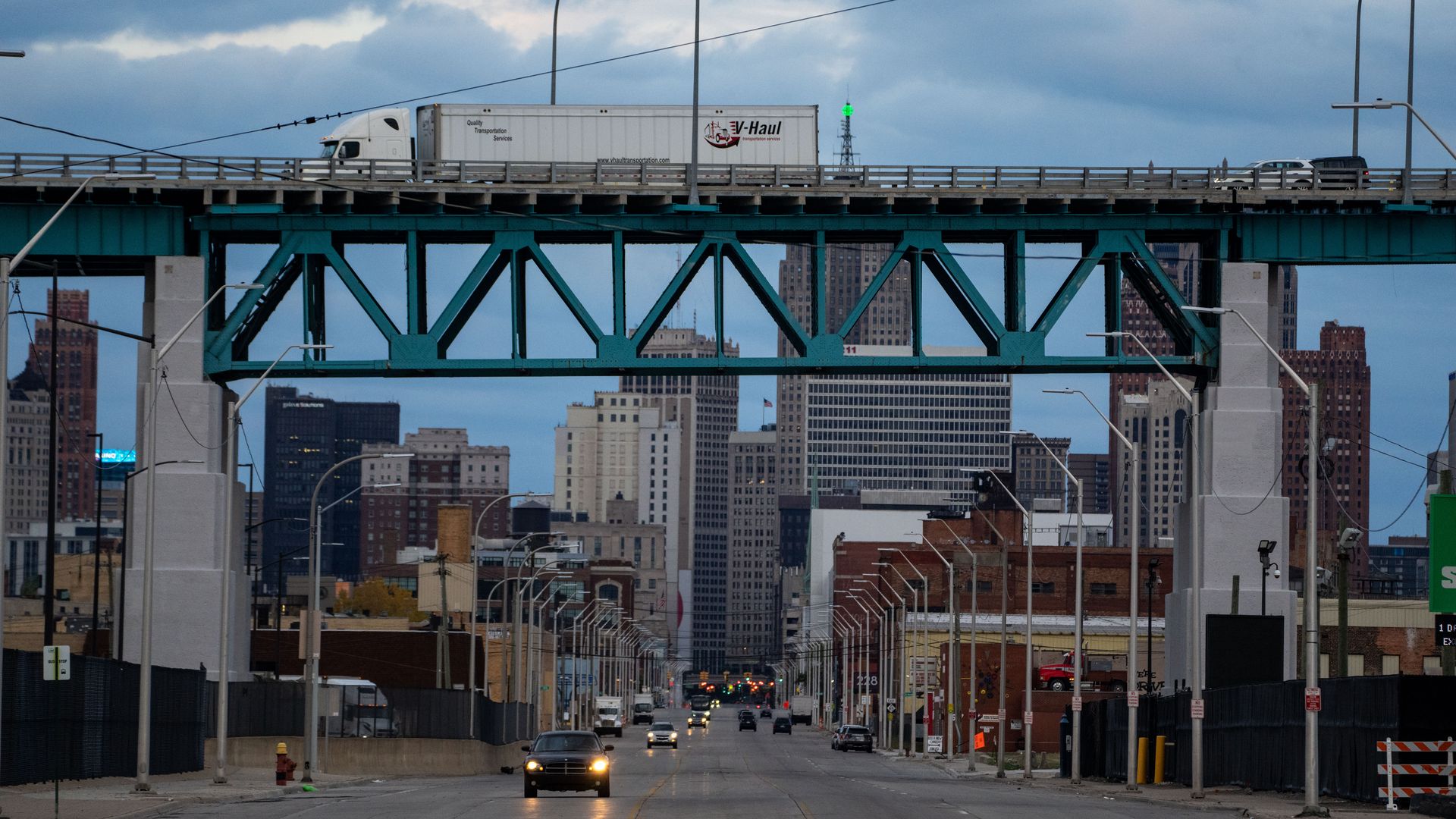 car drives along a city street of detroit as a truck drives on a bridge overhead