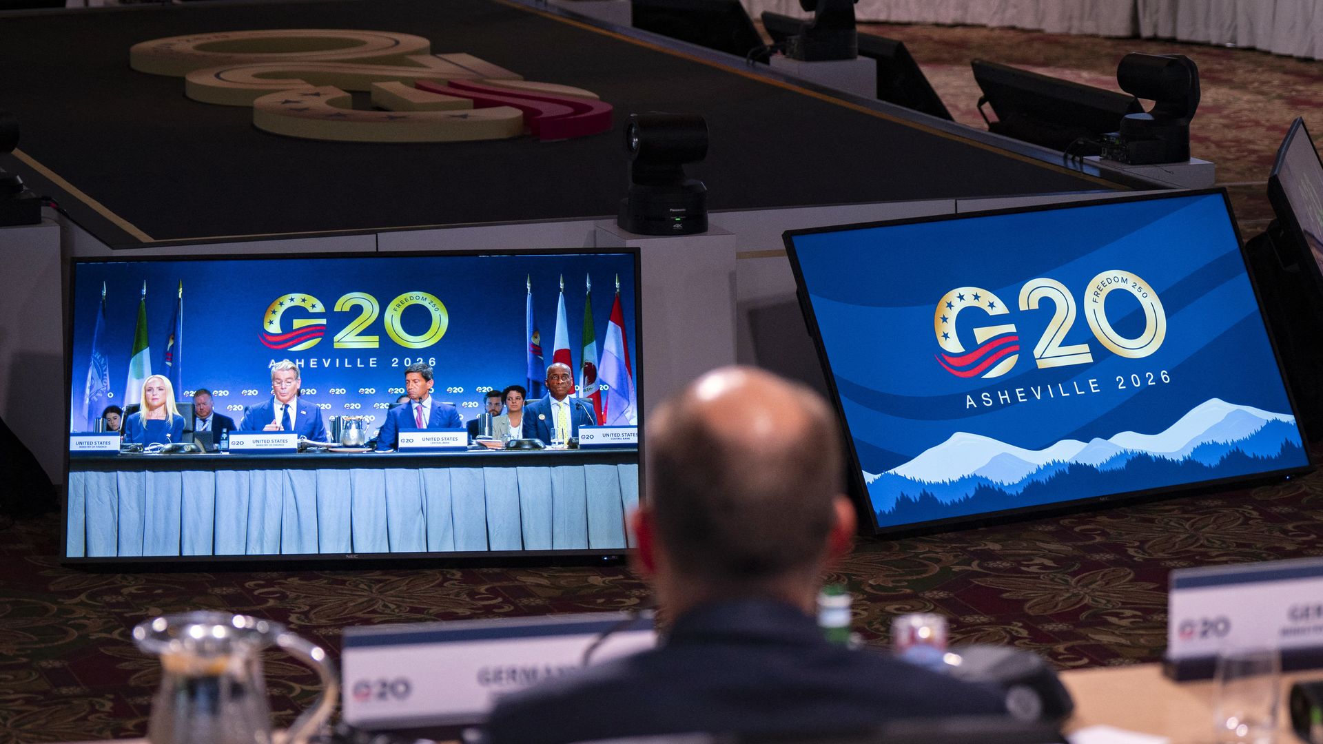 An attendee watches a screen showing the US Treasury Secretary Scott Bessent  and the US delegation 