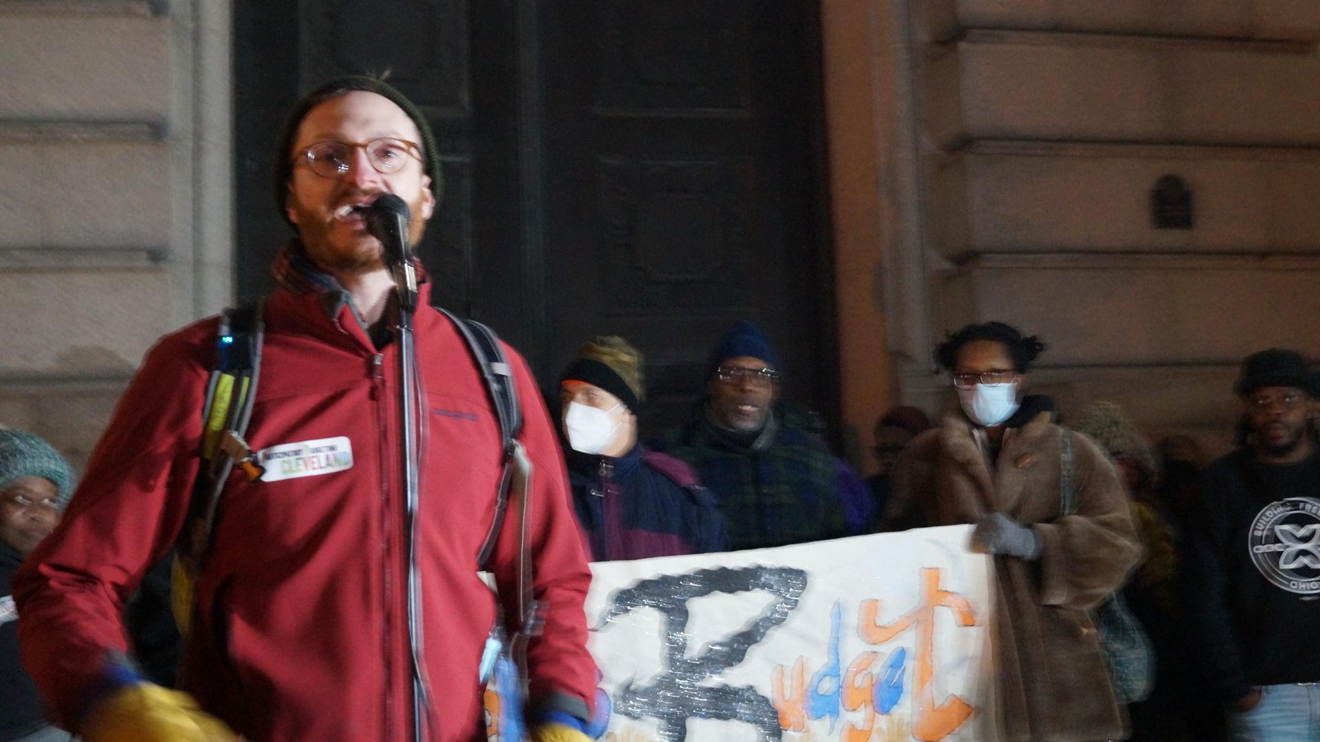 An organizer in winter gear speaks at a microphone outside Cleveland City Hall 