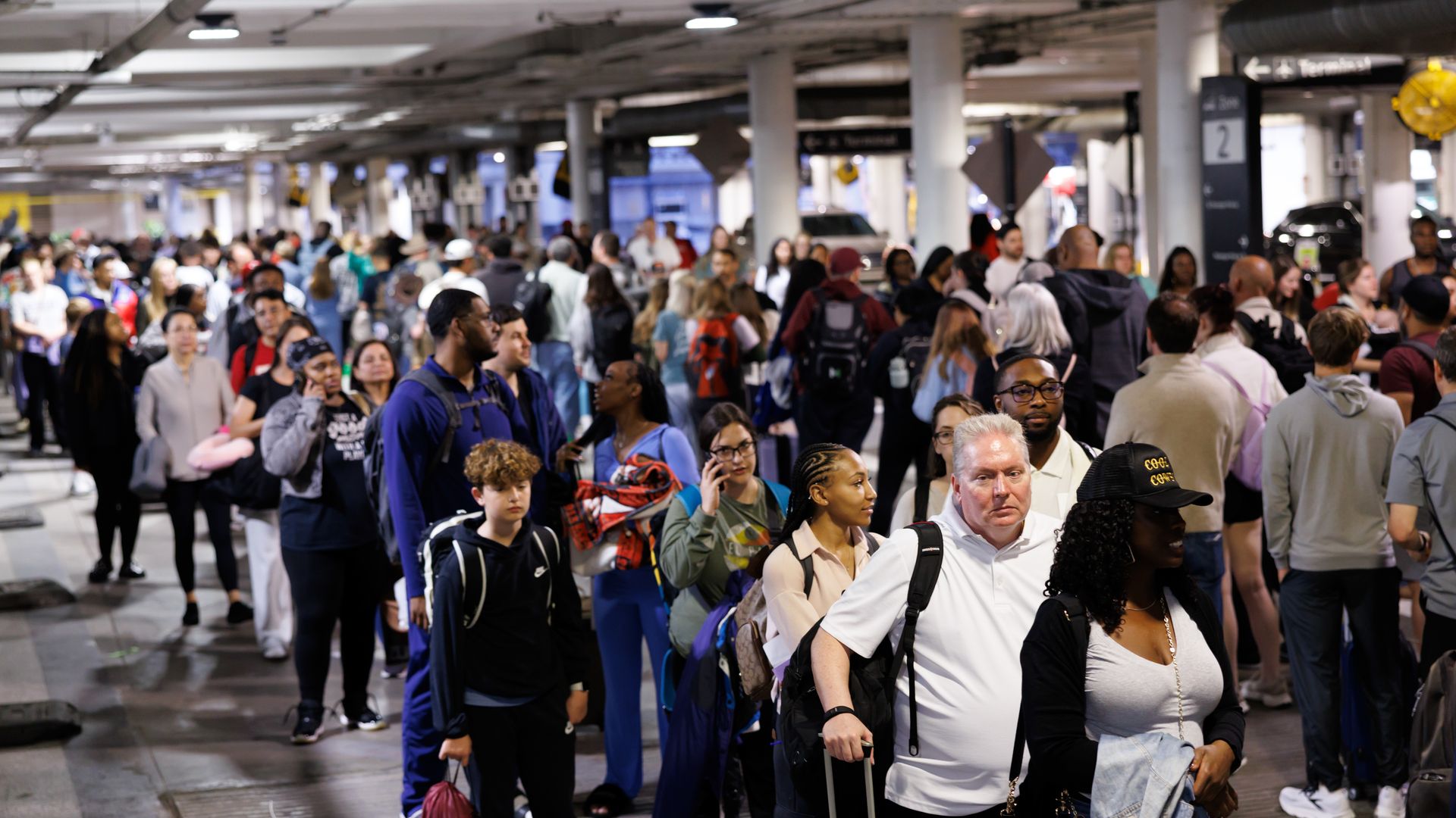 Travelers wait in a long line at a TSA checkpoint. Some wear backpacks or carry bags or suitcases.