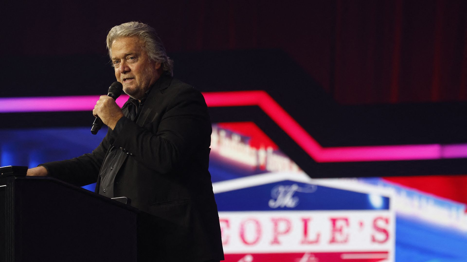 Steve Bannon stands speaking into a microphone that he is holding 