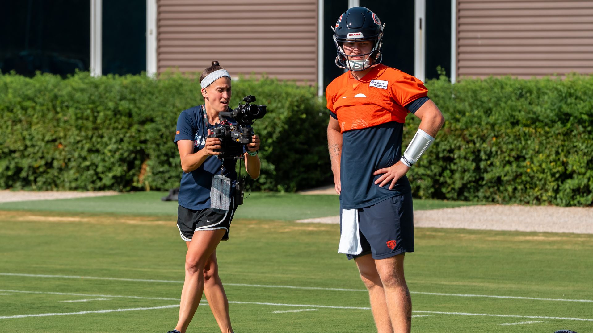 Photo of a woman with a camera taking photos of a football player on a field 