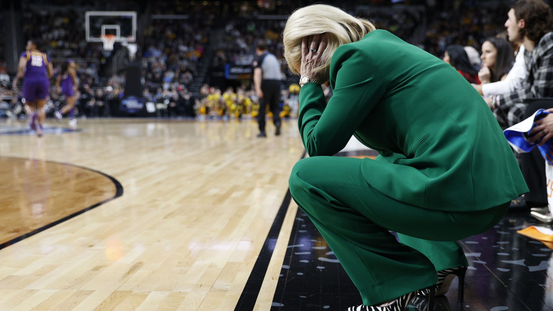 Kim Mulkey kneels with her head in her hands on the sideline during an LSU v. Iowa game.