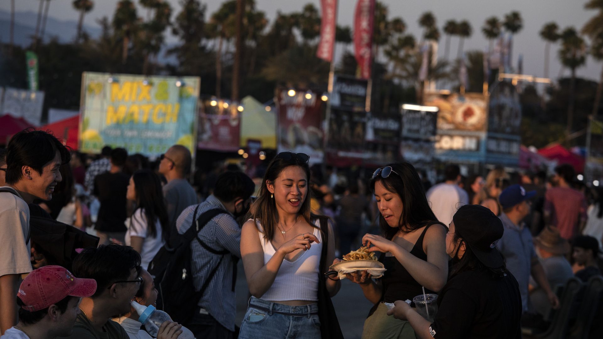 A group of young women eat street fair food in a crowd at the 626 Night Market.