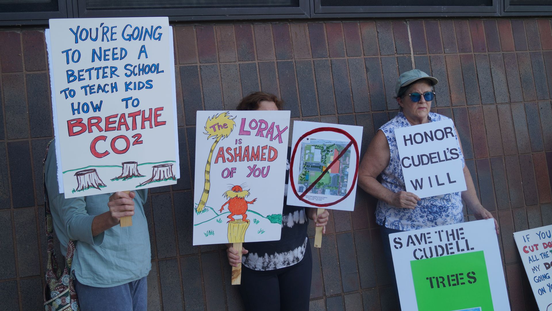 Cleveland residents hold signs in support of Cudell Park mature trees outside brick building