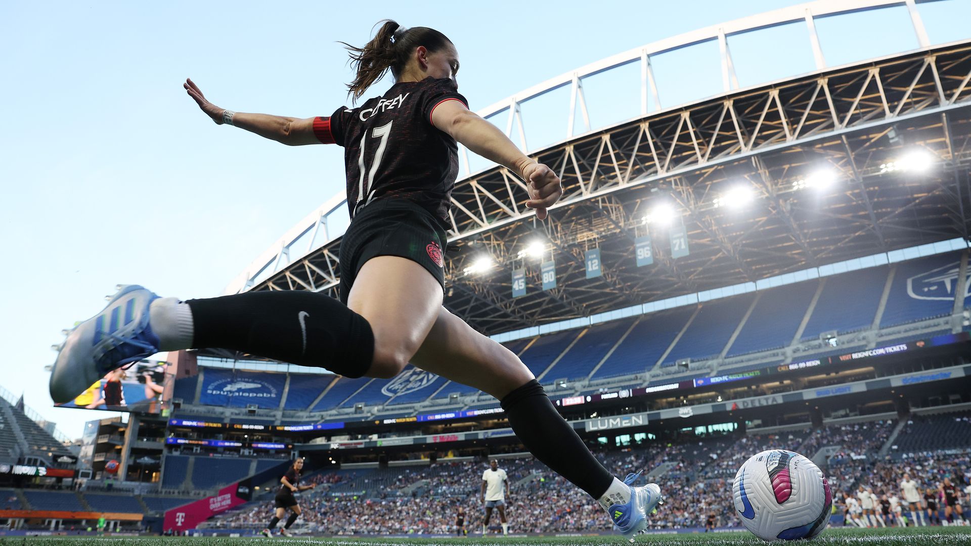 Soccer player with "COFFEY" on black jersey prepares to kick ball inside large stadium with blue seats and bright lights overhead.