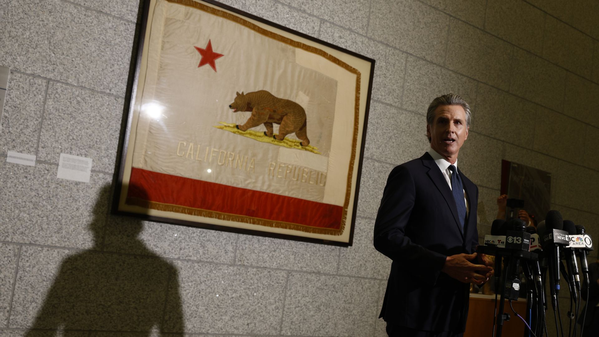 Gov. Gavin Newsom at a lectern for a pres conference. A California flag is behind him framed. 