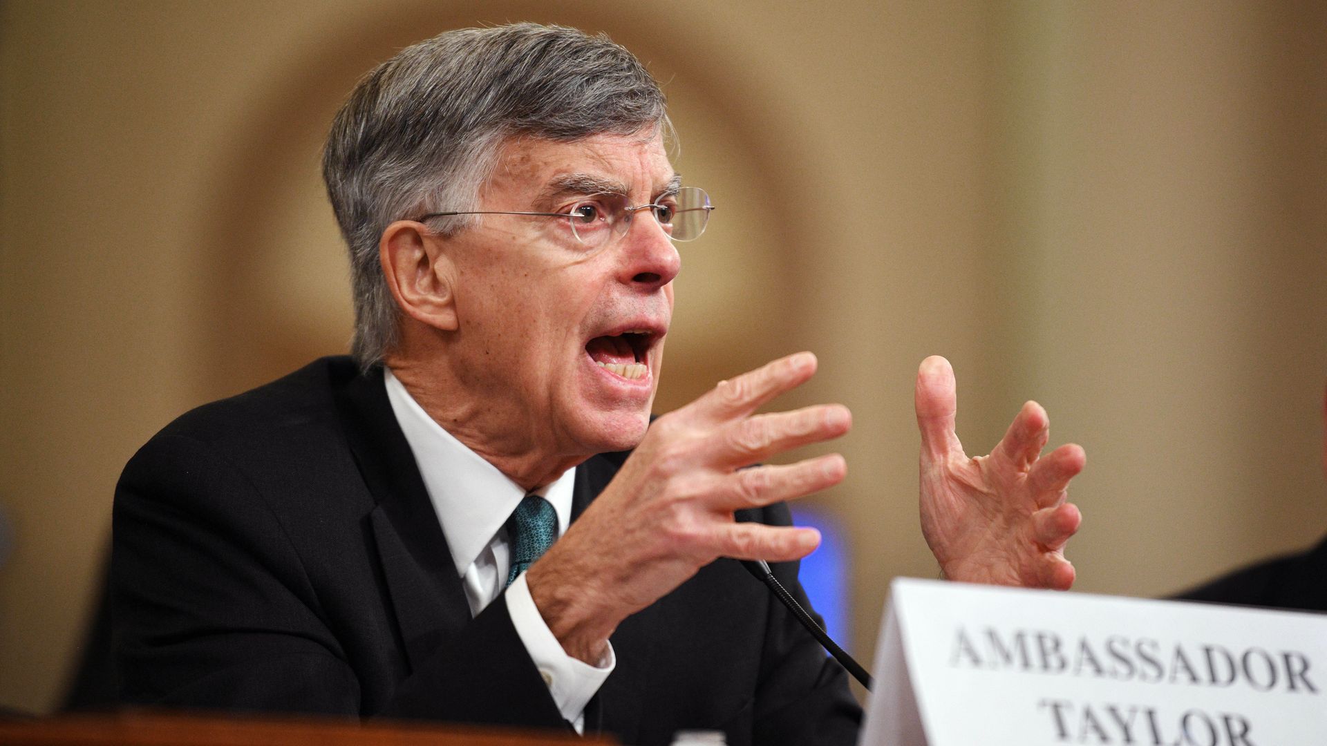 In this image, Taylor sits and speaks while talking with his hands