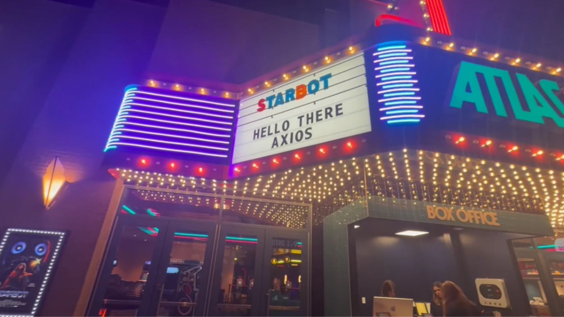 Brightly lit movie theater entrance at night with marquee reading \