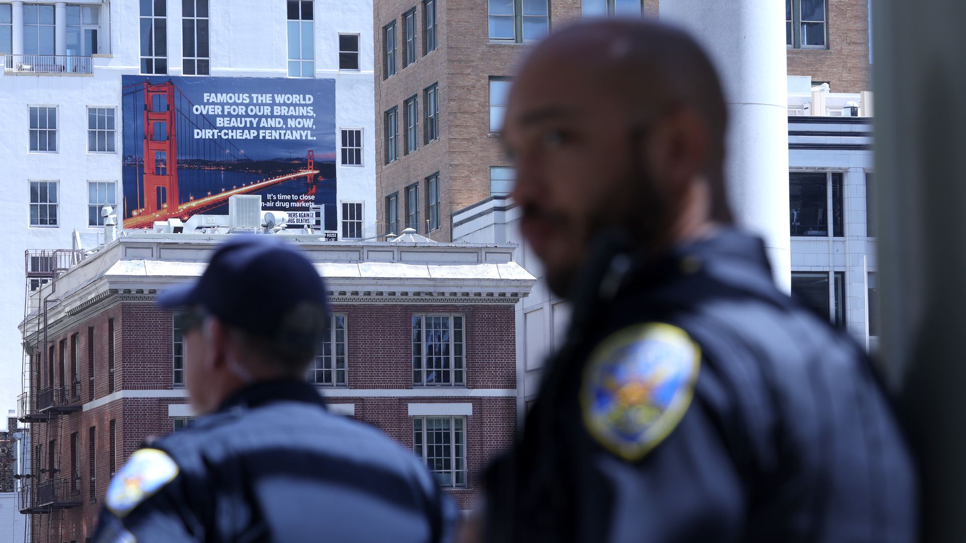 Photo of a billboard that shows the Golden Gate Bridge and text that says: "Famous the world over for our brains, beauty and now, dirt-cheap fentanyl." Two SFPD officers are in the foreground of the photo.