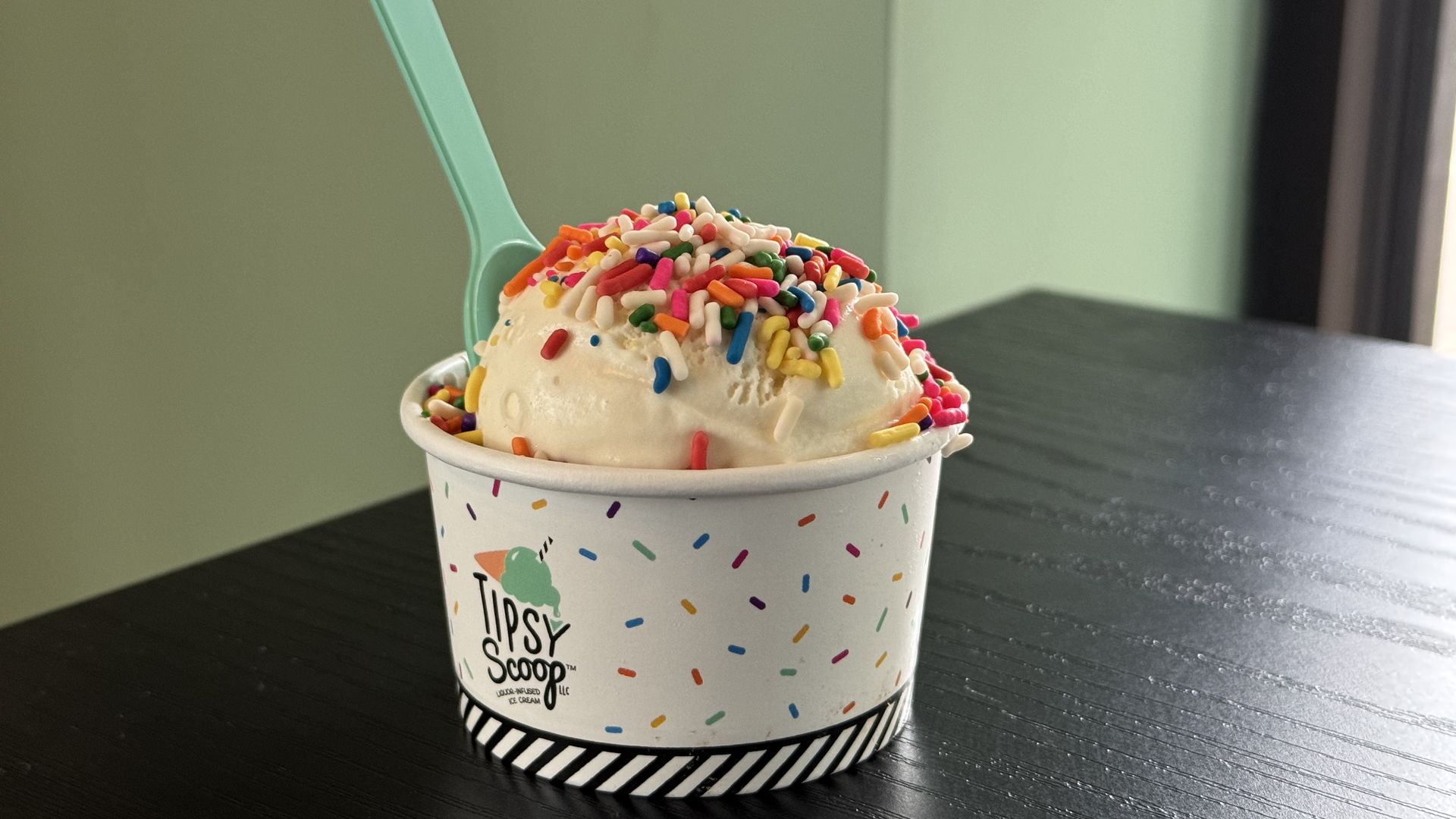 A scoop of ice cream with sprinkles is seen in a cup with the words "Tipsy Scoop" on the side.